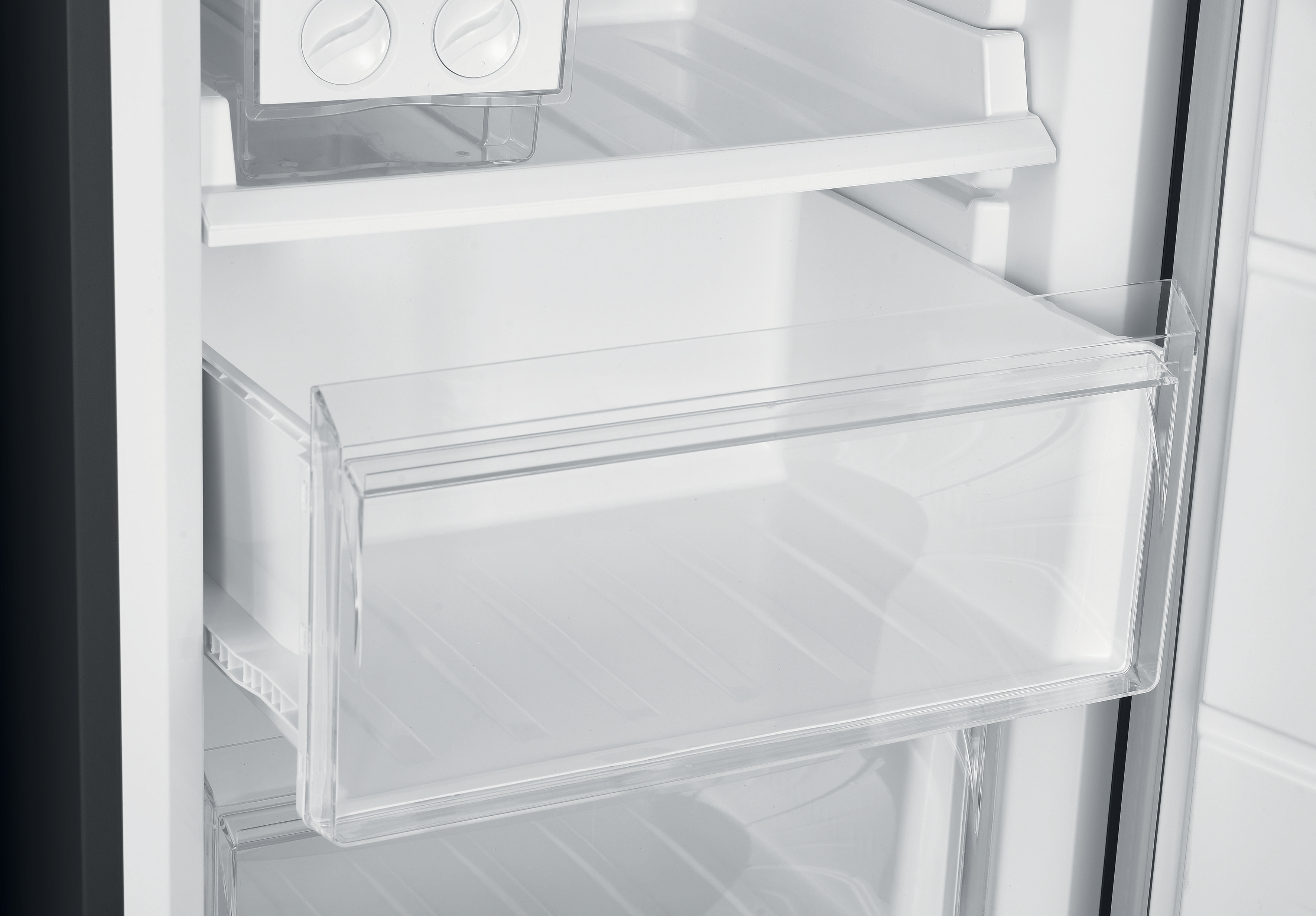 Dentro de un refrigerador, mostrando estantes blancos y un cajón transparente.