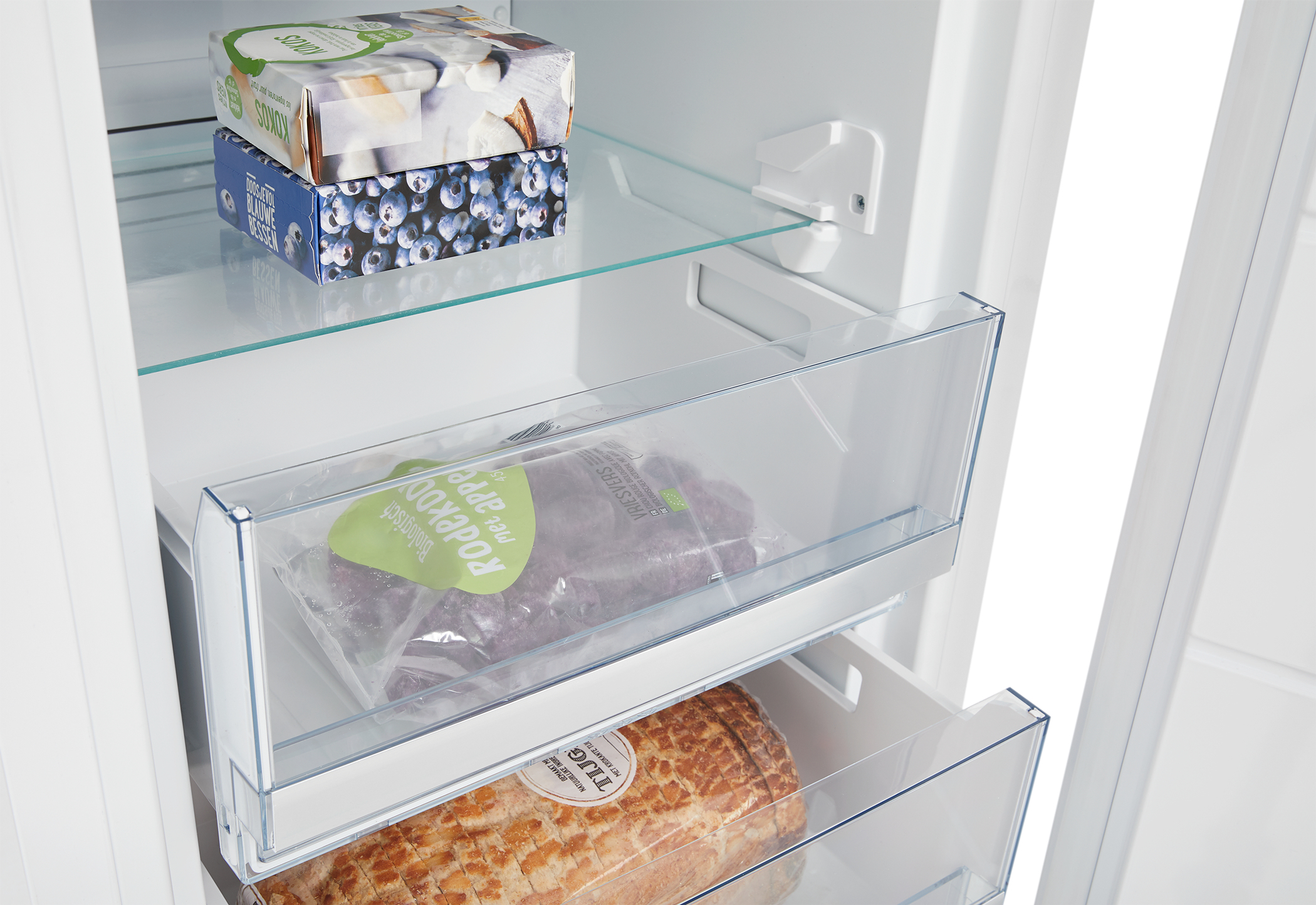 Interior de nevera con alimentos. La repisa superior tiene cajas, la del medio una bolsa de productos y la inferior un pan.