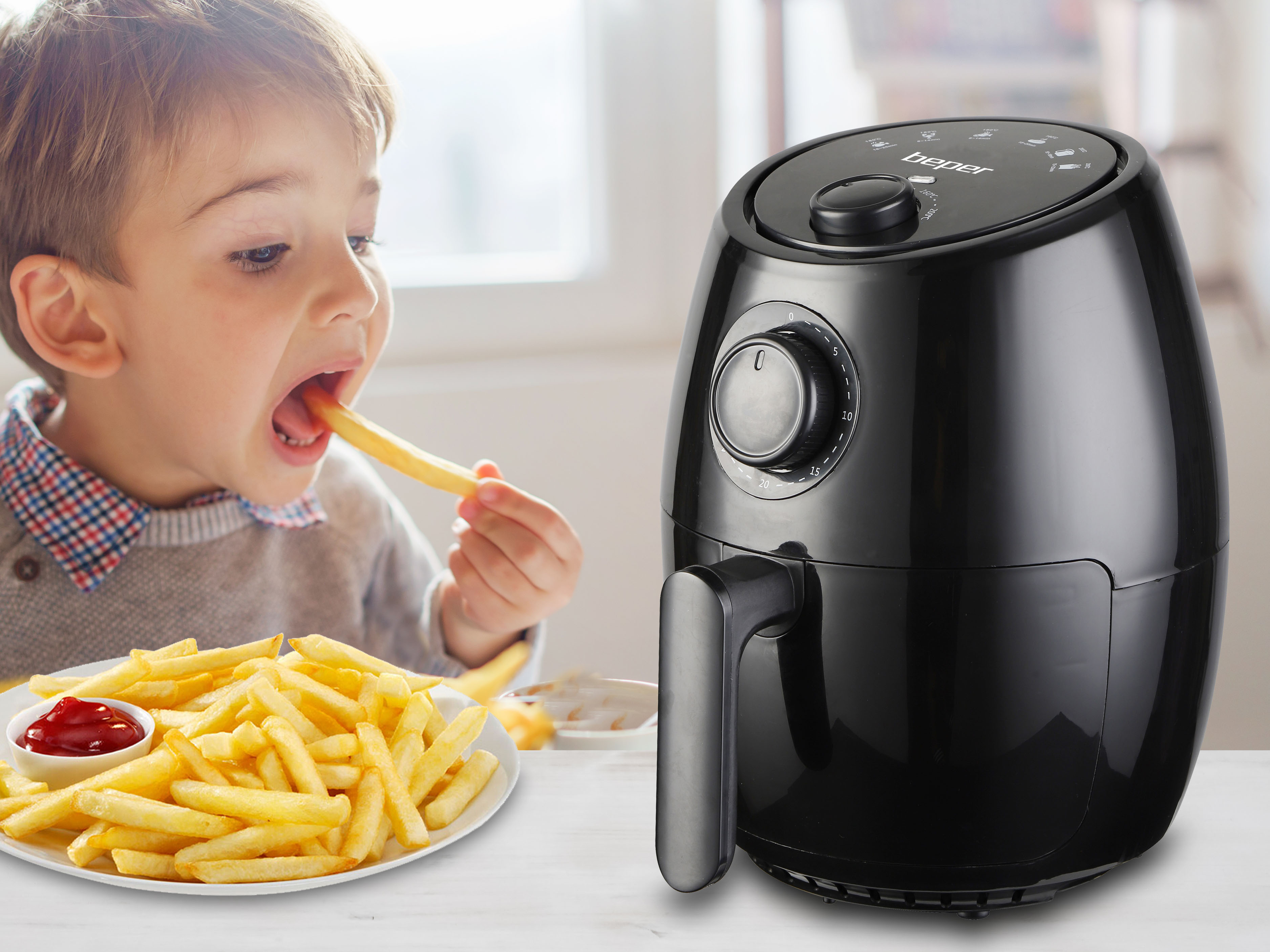Un bambino mangia una patatina fritta vicino a una friggitrice ad aria nera, con patatine e ketchup sul tavolo.