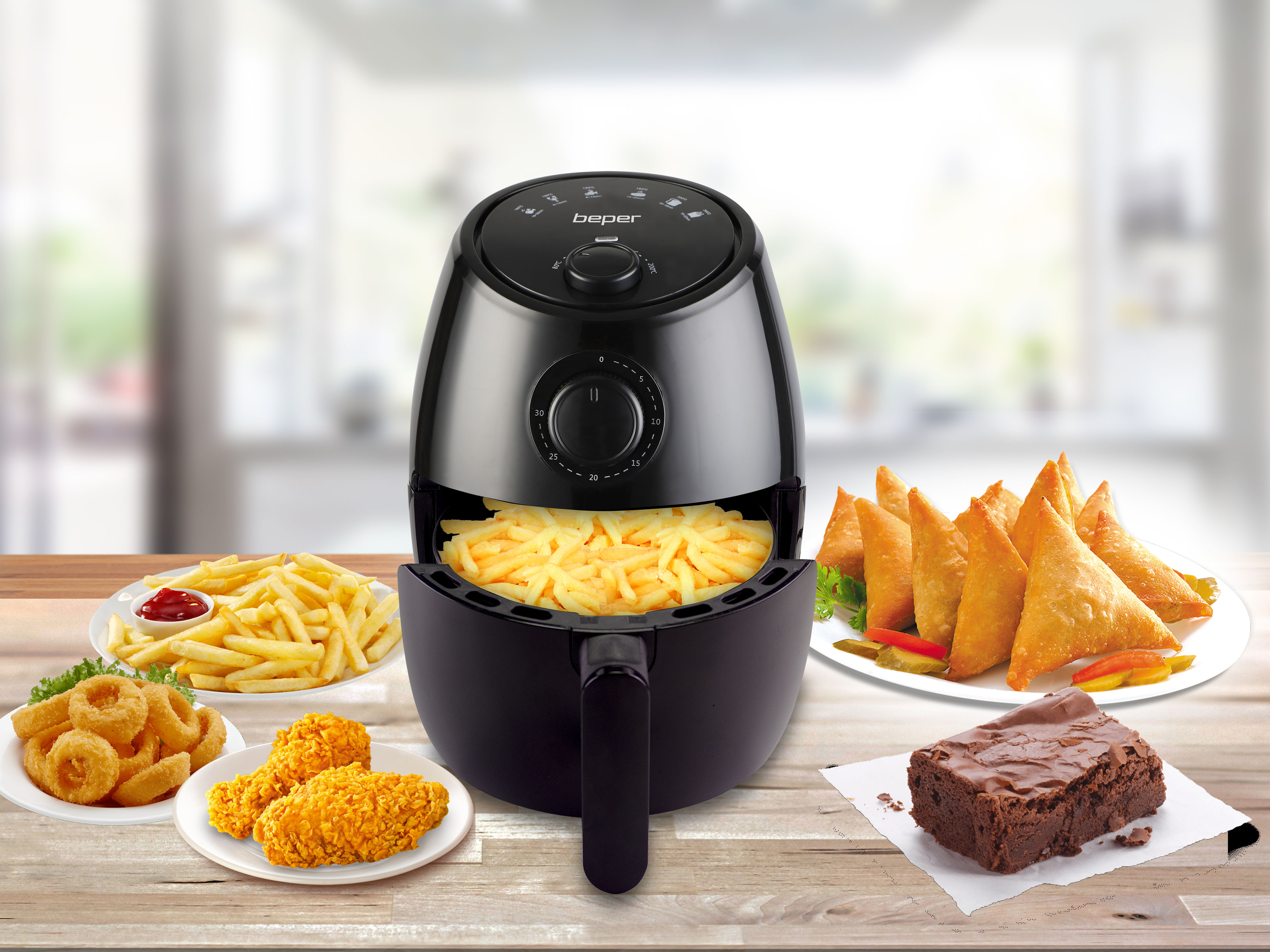 Una friggitrice ad aria nera con patatine fritte, snack fritti e un brownie su un tavolo di legno. Lo sfondo è sfocato.