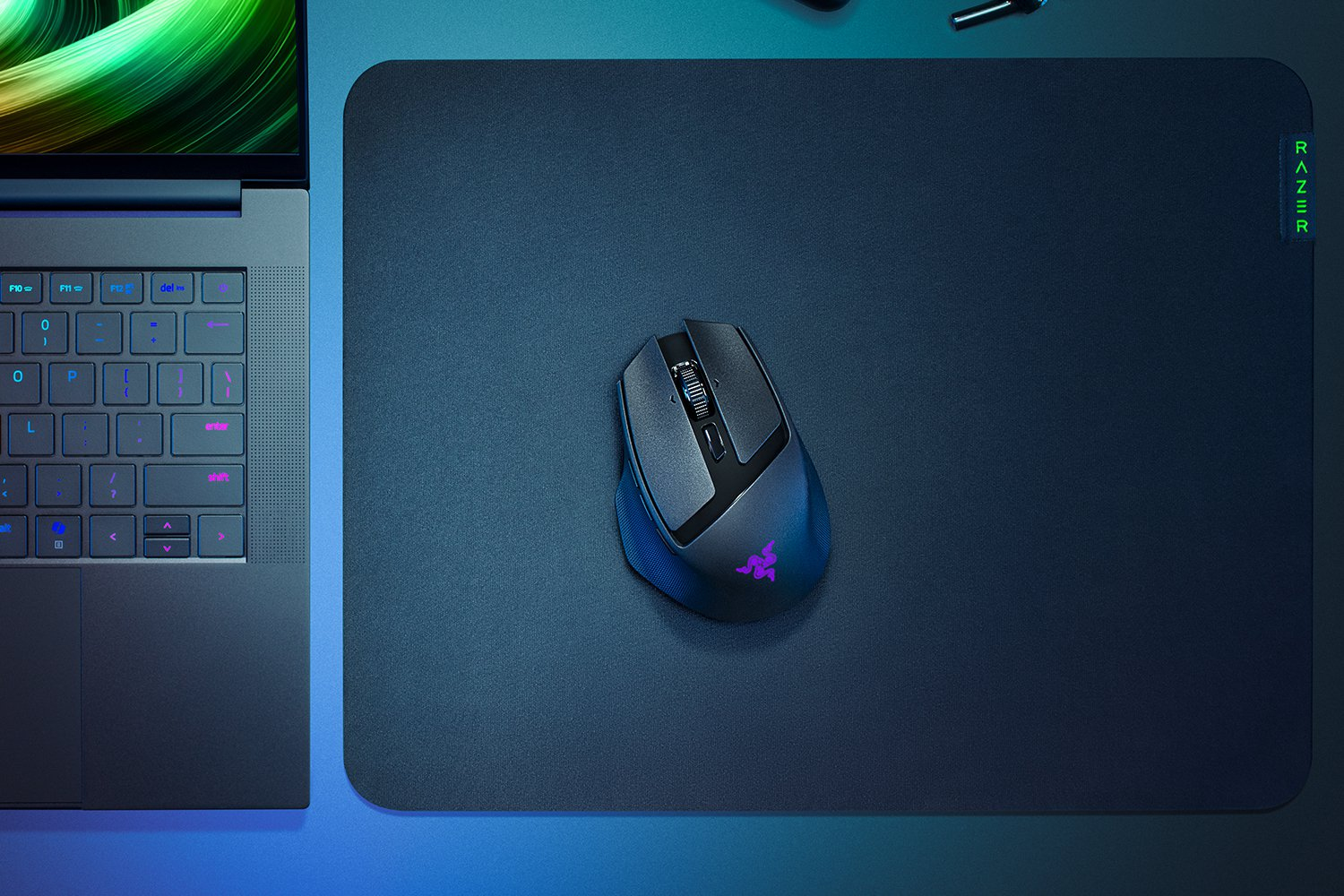 Mysz do gier na podkładce obok klawiatury laptopa. Mysz jest czarna i ma świecące logo Razer.