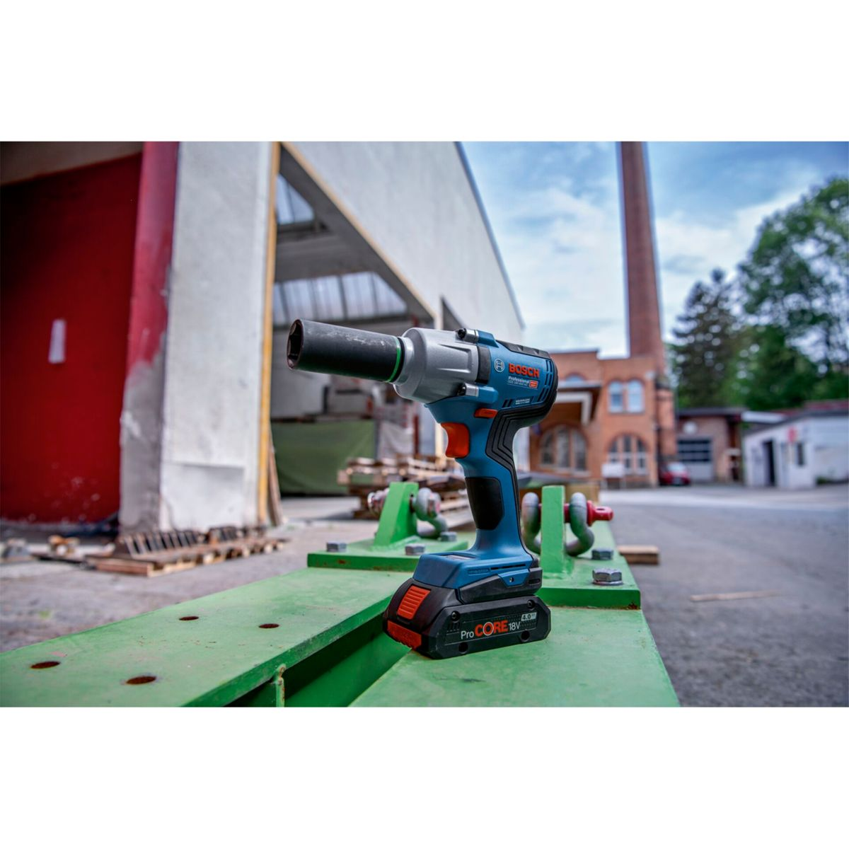 Niebiesko-czarny klucz udarowy Bosch leży na zielonej metalowej powierzchni. Budynki i komin w tle.