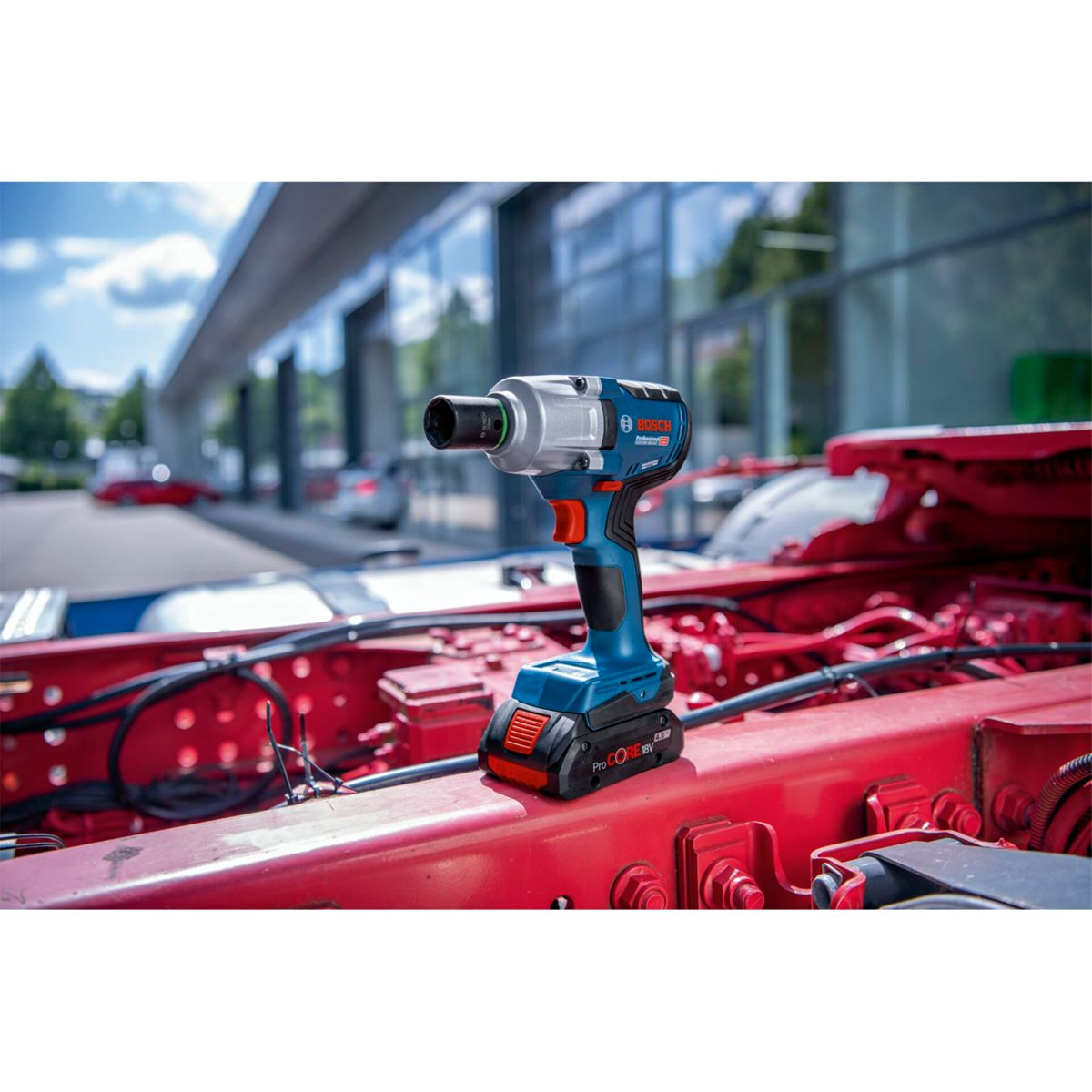 Niebiesko-srebrny klucz udarowy Bosch na czerwonej ramie ciężarówki. W tle budynek i niebo.