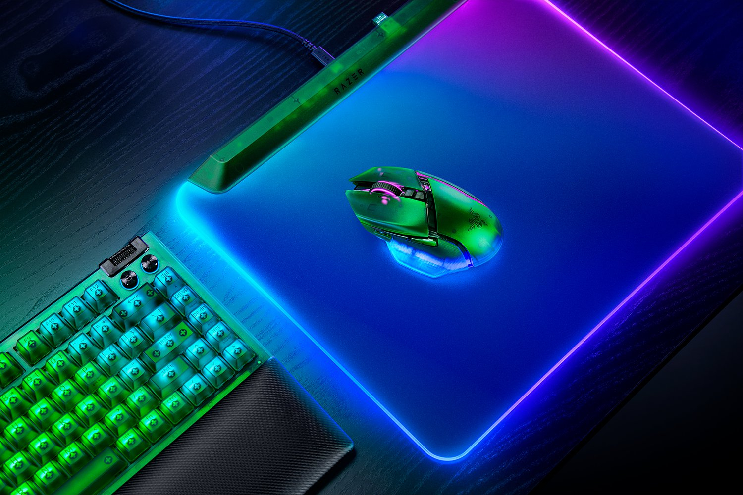 Konfiguracja do gier z zieloną myszką, klawiaturą i podkładką pod mysz podświetlaną na niebiesko i fioletowo. Widoczne logo Razer.