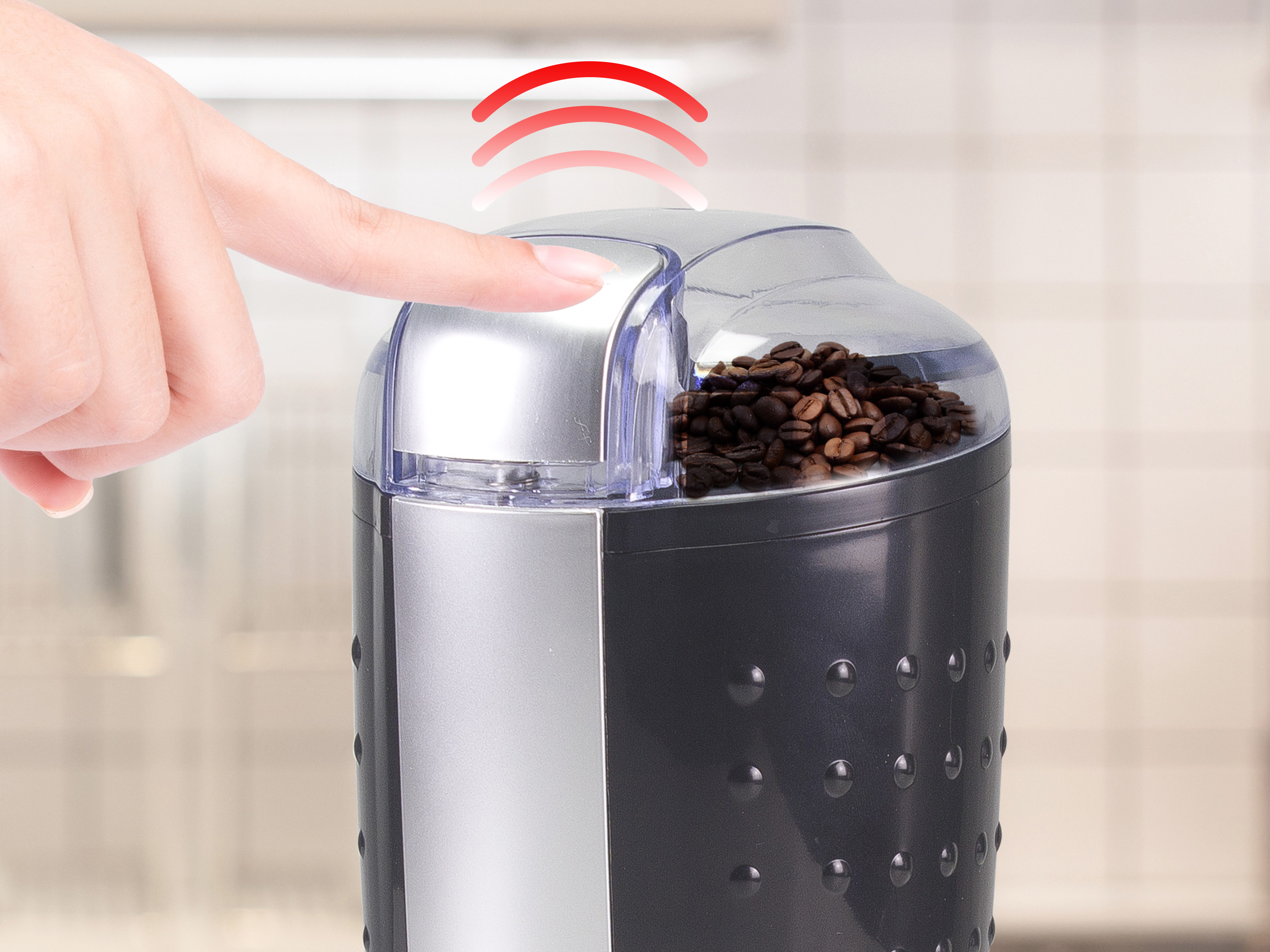 Palec naciska przycisk młynka do kawy. Czerwone fale nad nim. Ziarna w przezroczystej górze.