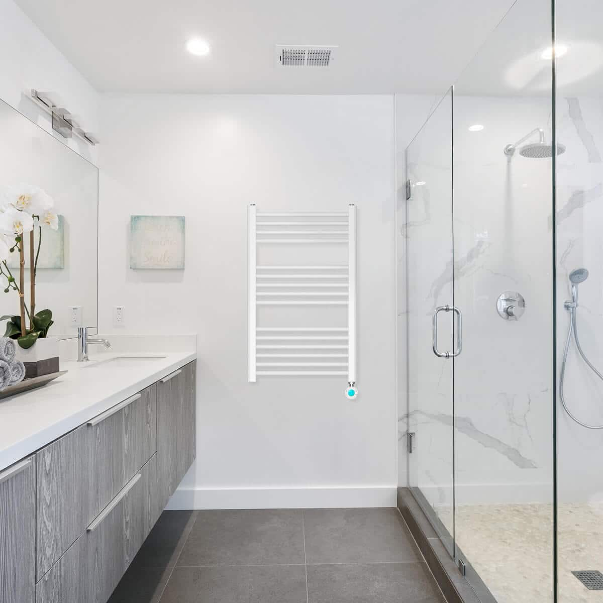 Nowoczesna łazienka z białym podgrzewaczem ręczników, prysznicem i toaletką. Szare płytki podłogowe i szare drewniane szafki.