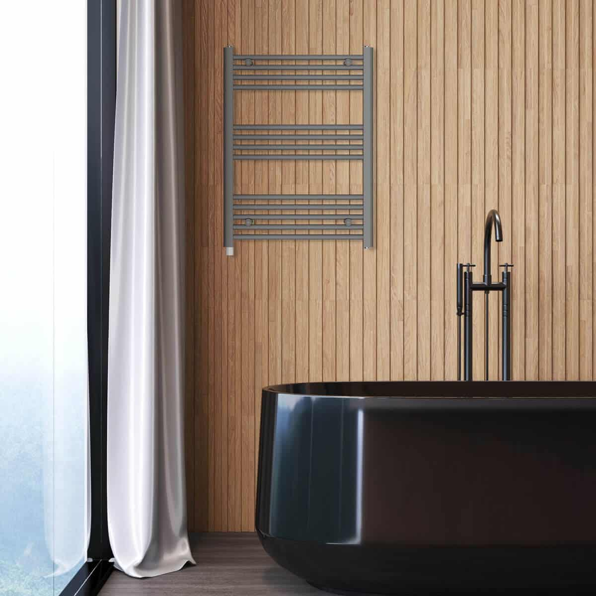 Łazienka z czarną wanną, szarym wieszakiem na ręczniki na drewnianej ścianie i czarną baterią. Okno z białymi zasłonami.