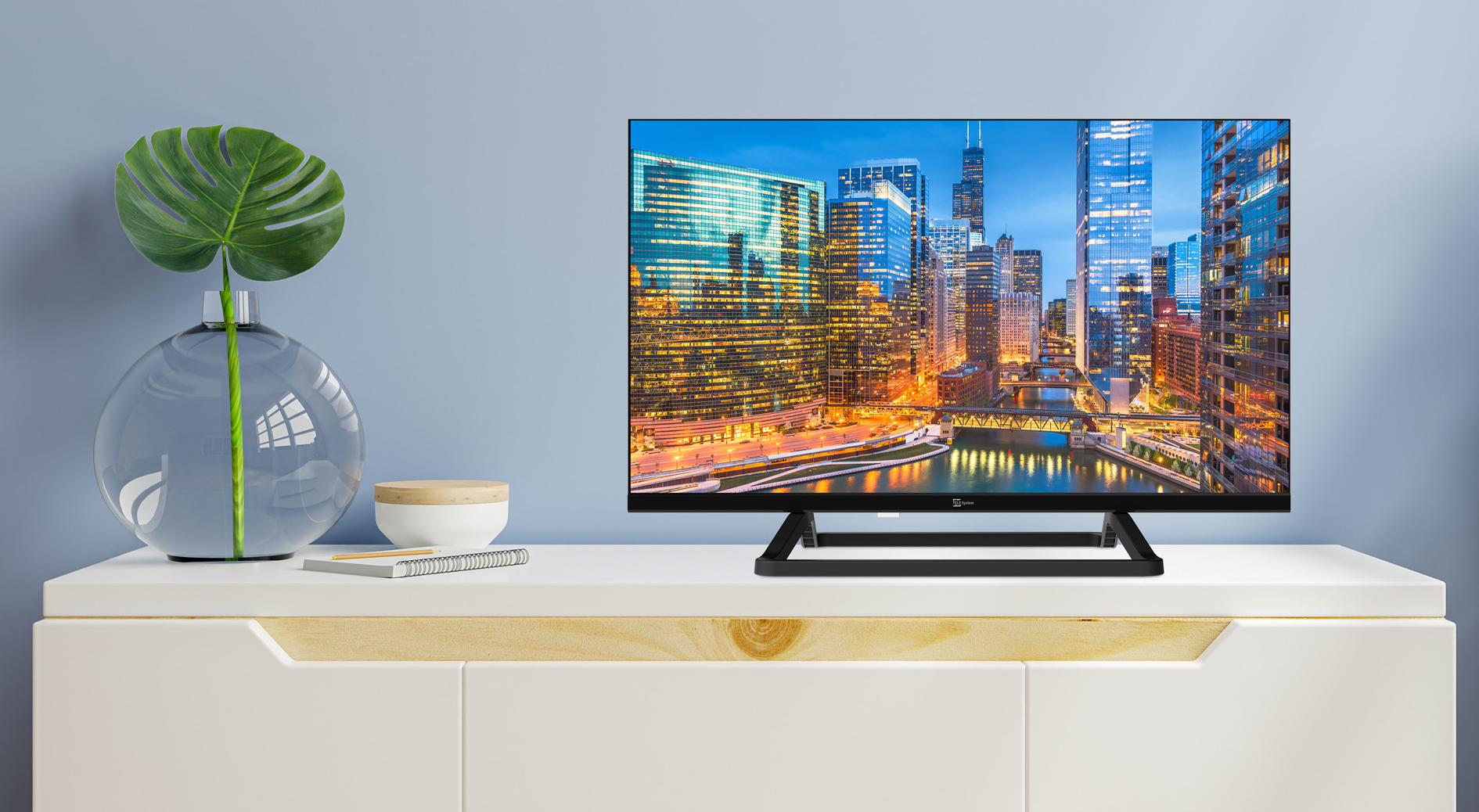 Una TV mostra lo skyline di una città. È su un mobile bianco con un vaso e una foglia. Lo sfondo è azzurro.