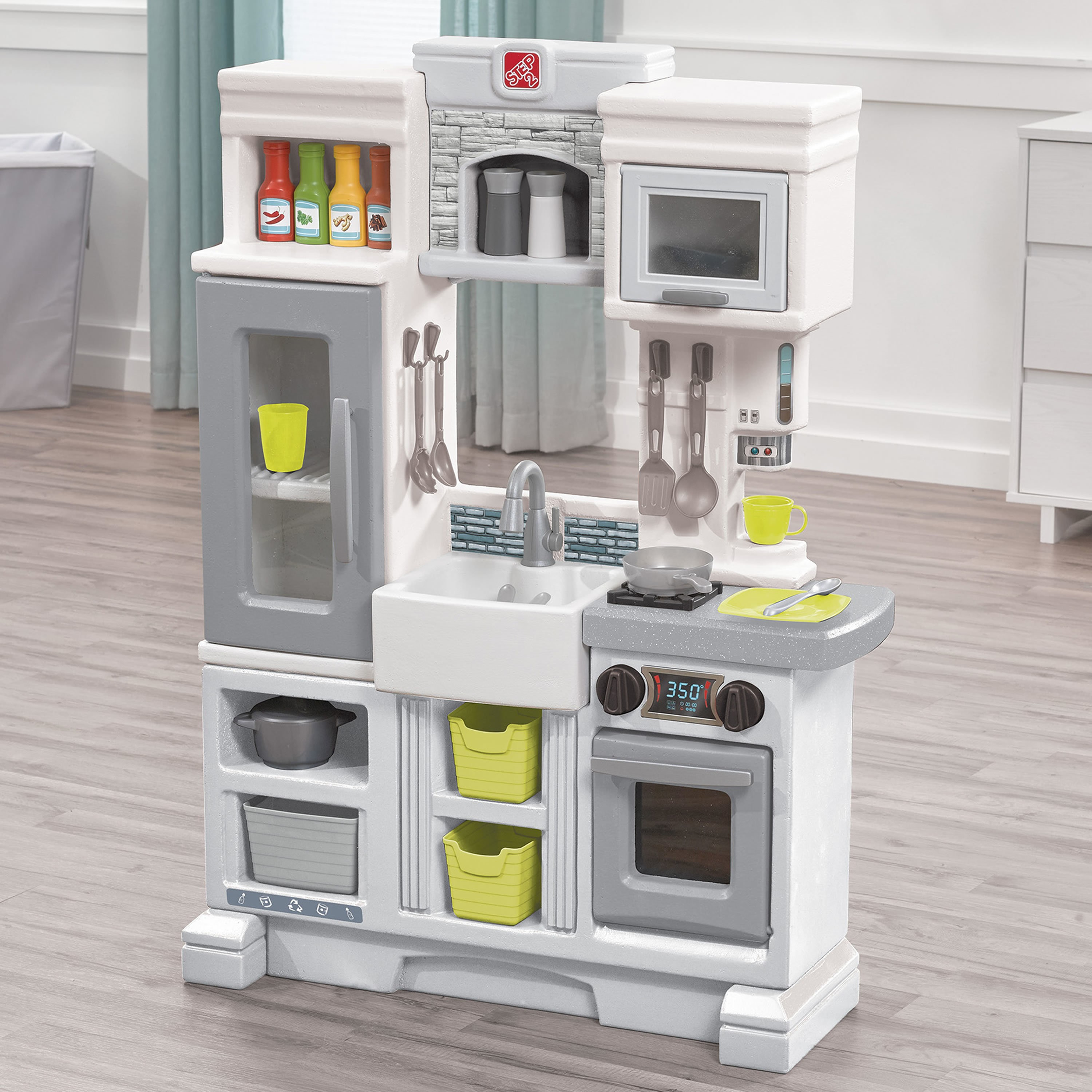 Ein Spielzeug-Küchenset mit Kühlschrank, Backofen, Mikrowelle und Spüle. Enthält Kochutensilien, Essensflaschen und eine Pfanne.