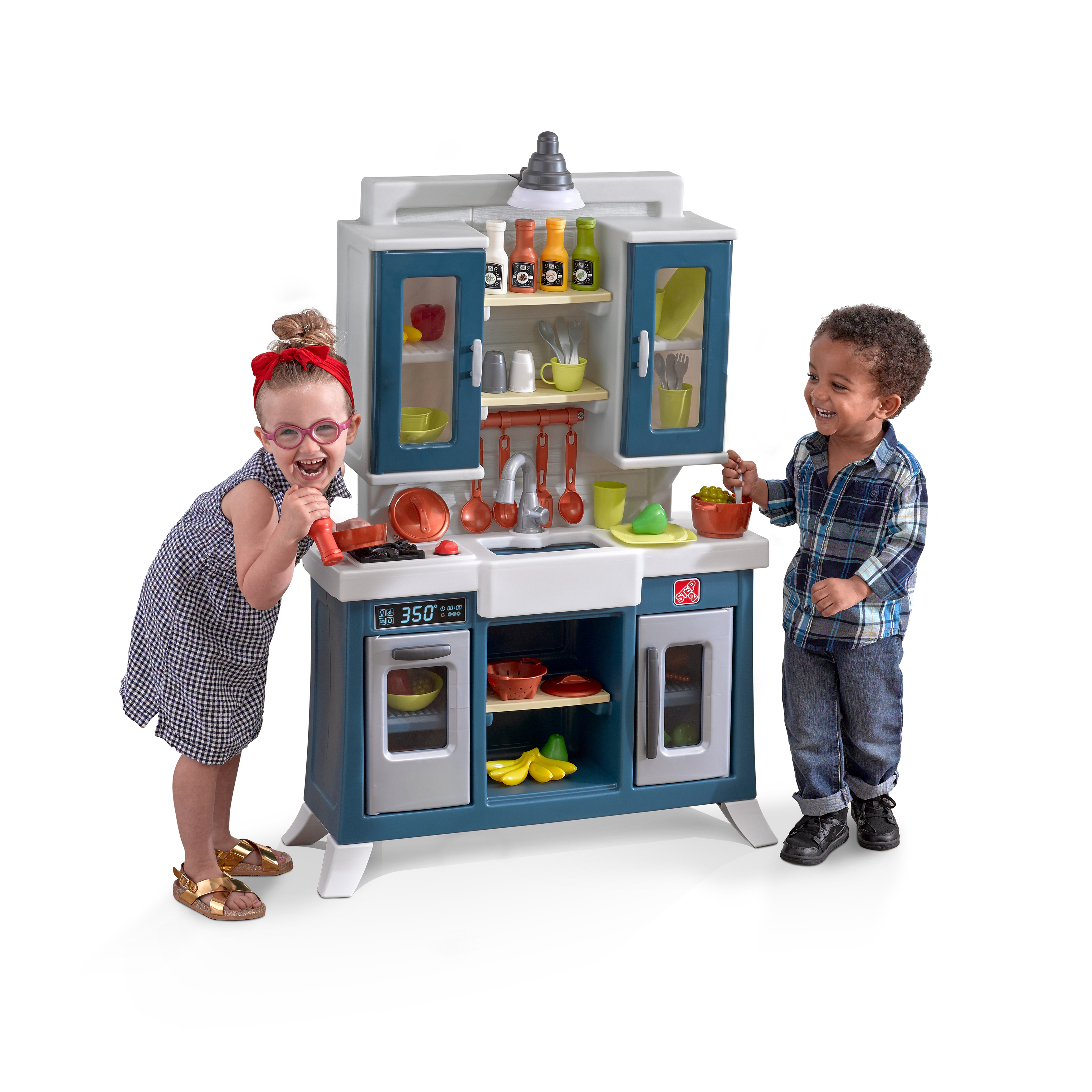 Zwei Kinder spielen mit einem Spielzeugküchenset. Ein Kind trägt eine Brille und eine rote Schleife. Das andere hat ein kariertes Hemd.