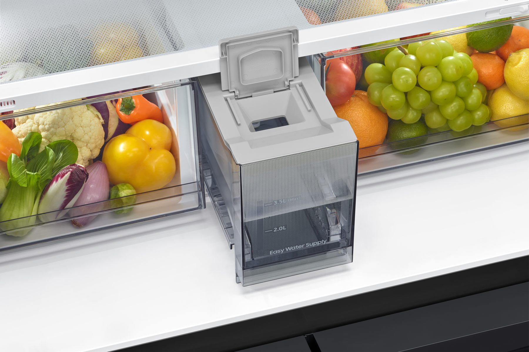 Interior de refrigerador con frutas y verduras en contenedores. Un dispensador de agua está en el centro. Los productos incluyen uvas, naranjas y pimientos.