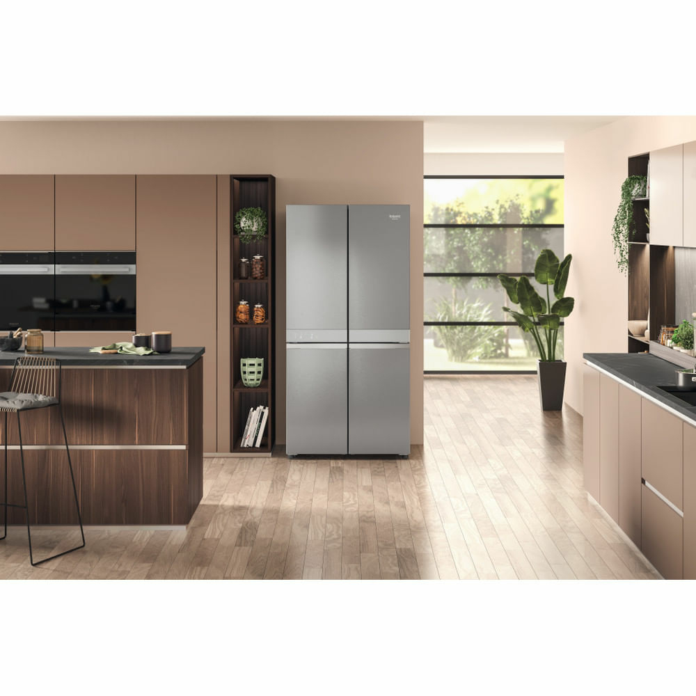 Una cucina moderna con un grande frigorifero grigio. I mobili e i pavimenti in legno completano lo schema di colori neutri. È visibile anche una pianta.