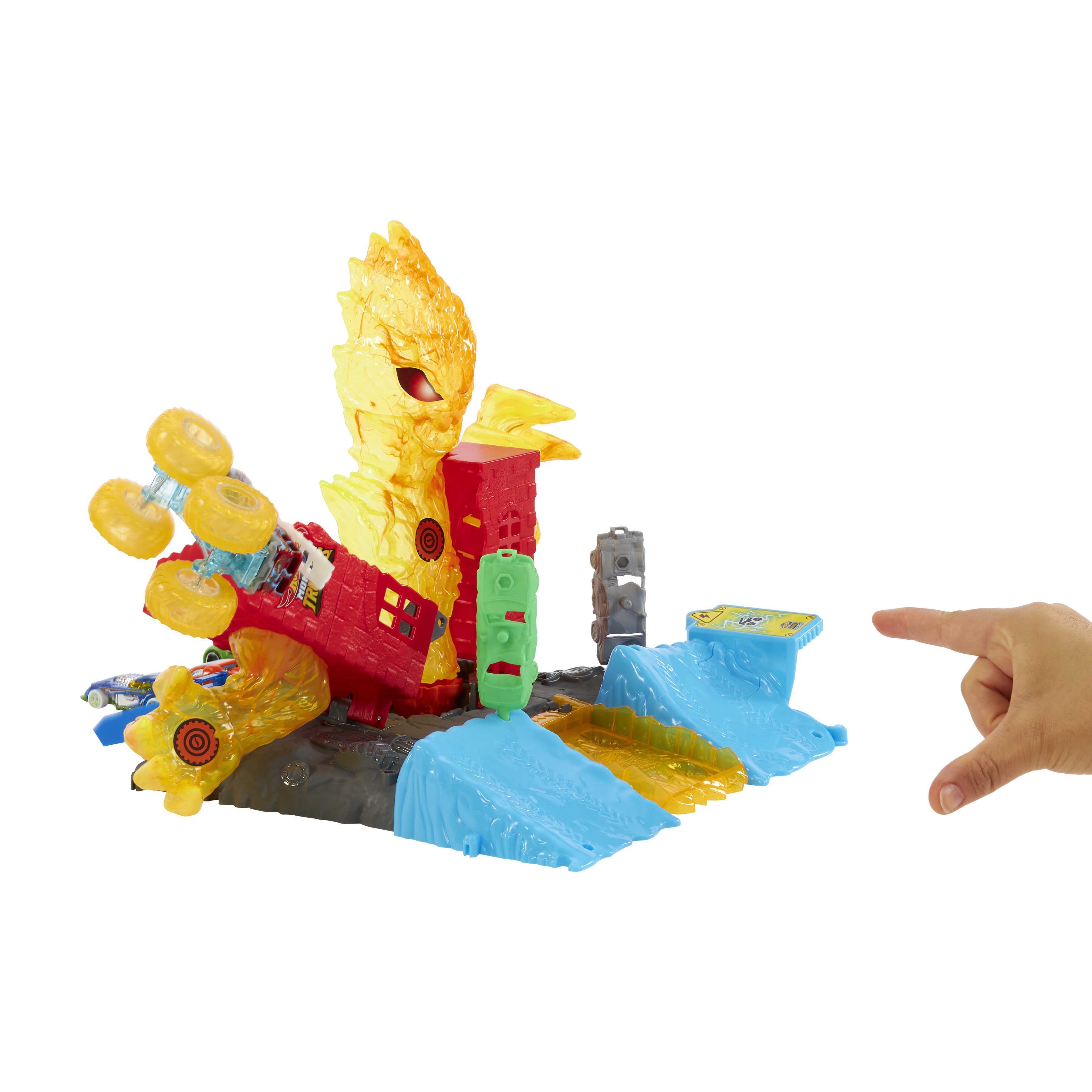 Ein Spielzeugset mit einer feuerroten Struktur, blauen Rampen und einem Monstertruck. Eine Hand zeigt auf das Set.