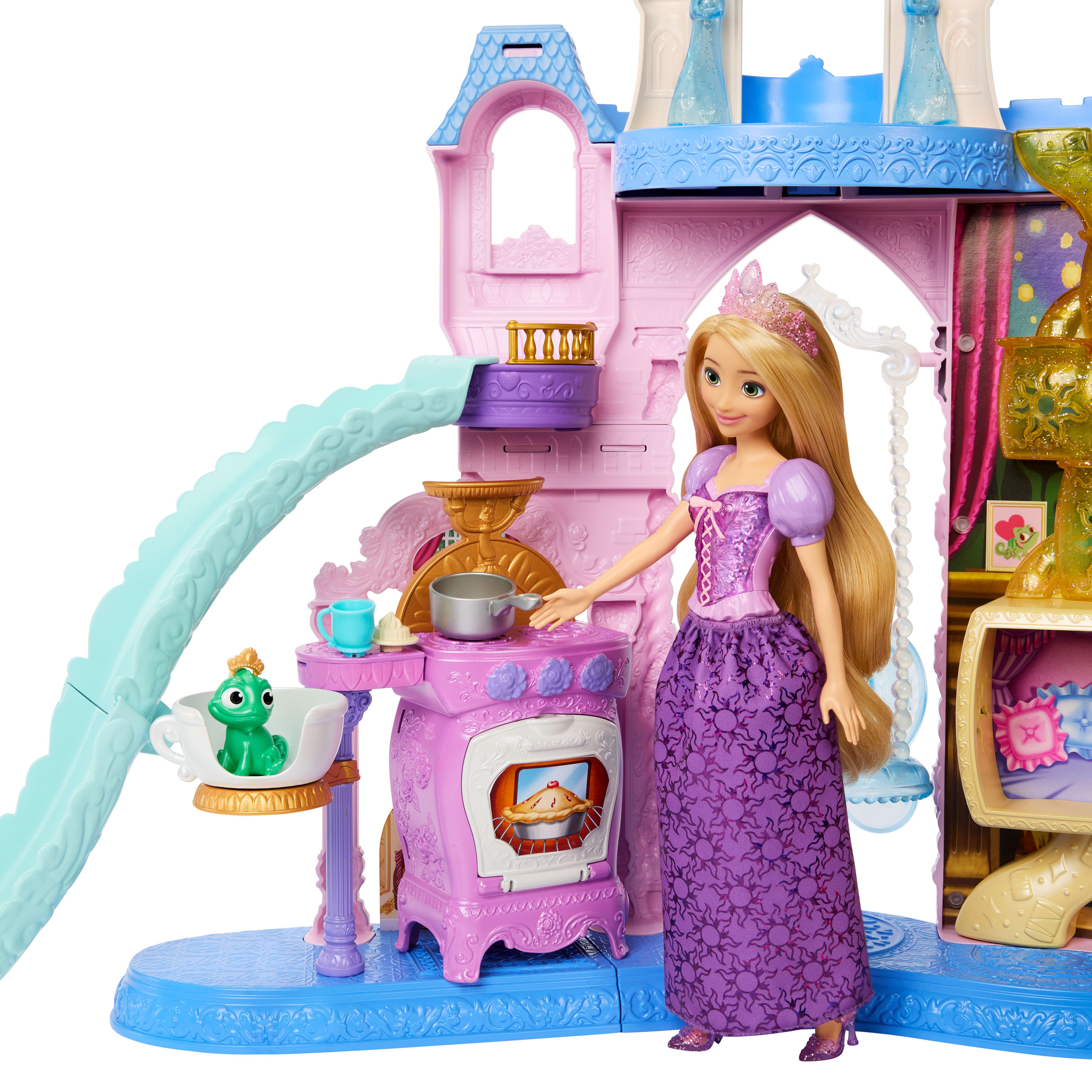Una muñeca Rapunzel está al lado de un juego de castillo rosa con un tobogán, una cocina y una rana verde en una taza de té.