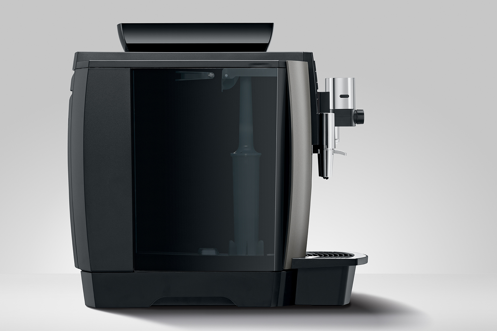 Eine schwarz-silberne Kaffeemaschine. Sie hat einen Wassertank, einen Auslauf und einen schwarzen Sockel. Der Hintergrund ist hellgrau.