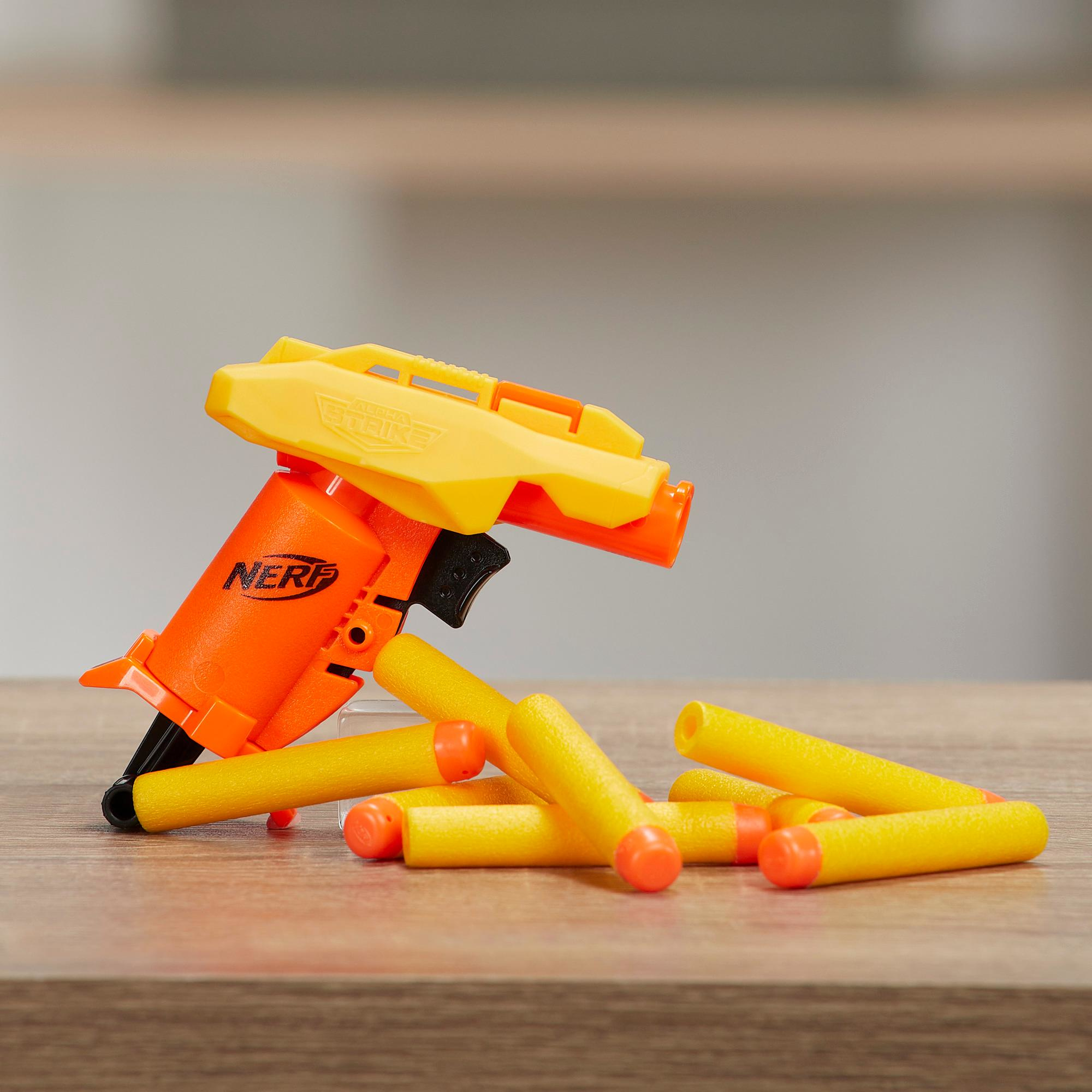 Eine orangefarbene und gelbe Nerf Alpha Strike Spielzeugpistole mit Darts auf einer Holzoberfläche. Hintergrund ist eine helle Wand.