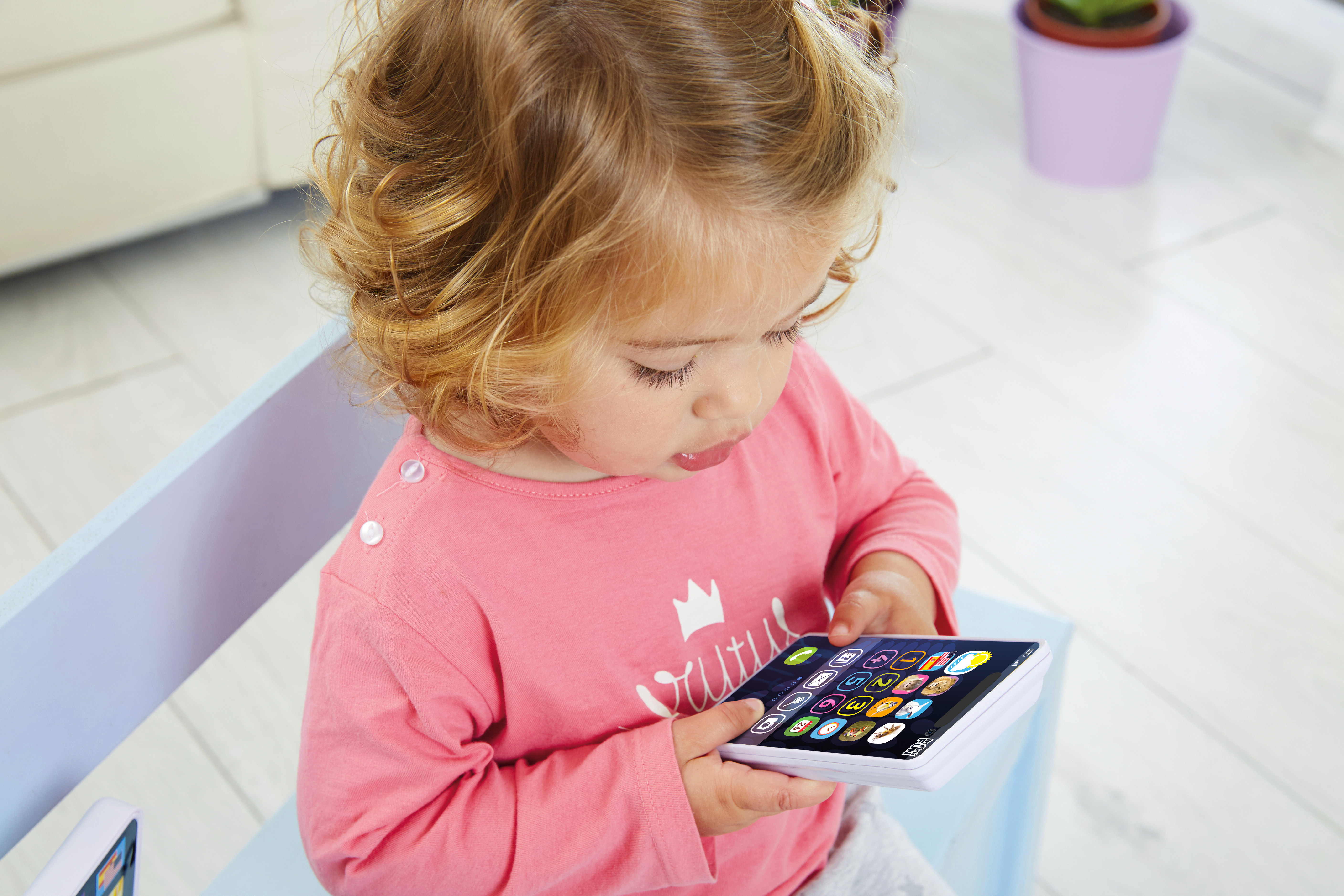 Un niño pequeño está sentado sosteniendo una tableta. Lleva una camisa rosa. La escena es en interiores.