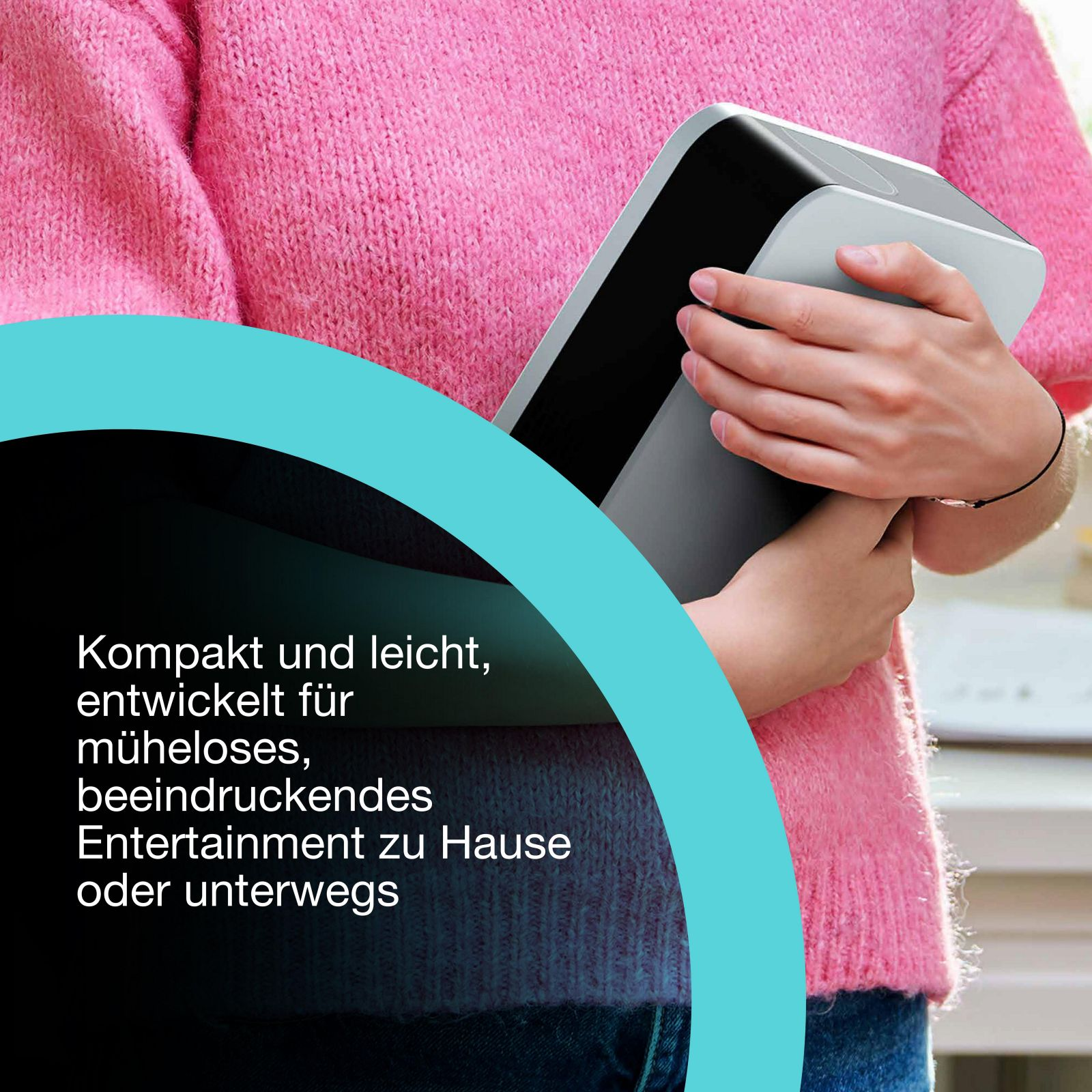 Osoba w różowym swetrze trzyma szare urządzenie. Tekst widoczny w lewym dolnym rogu.