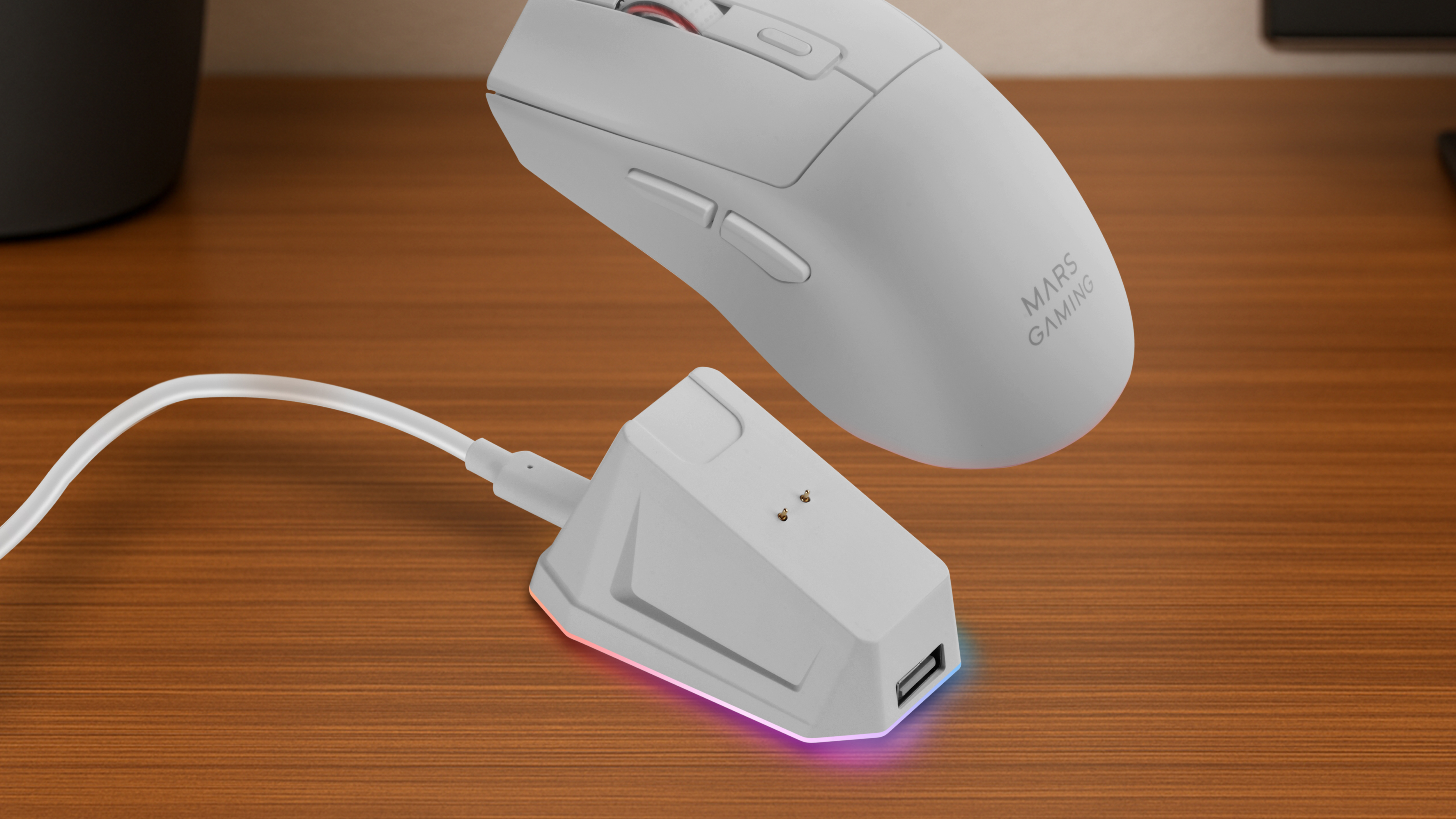 Een witte draadloze muis zweeft boven zijn oplaadbasis. De basis heeft een USB-poort en LED-verlichting. Beide staan op een houten bureau.