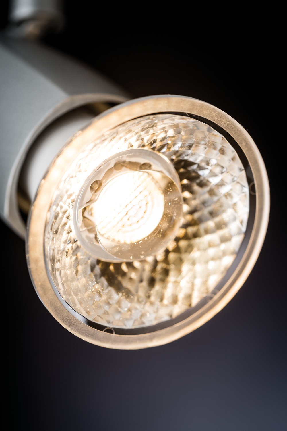 Zbliżenie podświetlonego reflektora. Żarówka jest jasna, otoczona teksturowaną soczewką. Tło jest ciemne.