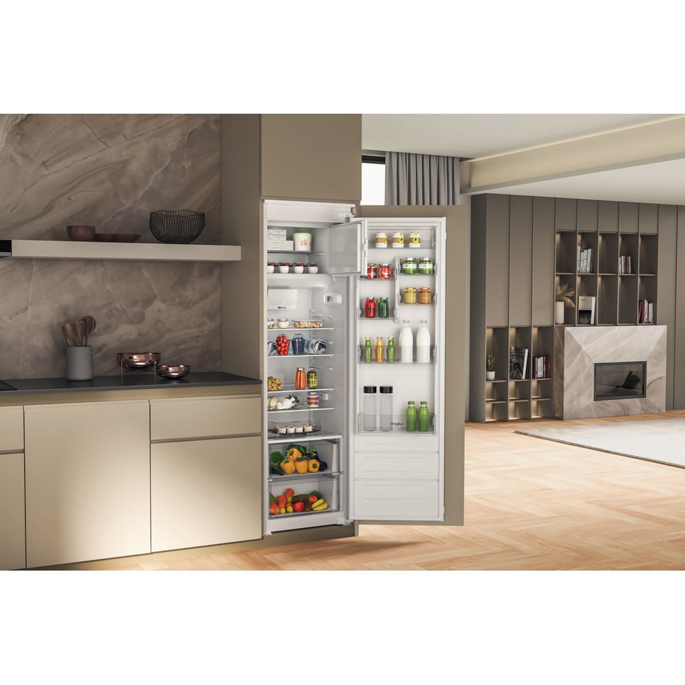 Un frigorifero aperto in una cucina moderna, pieno di cibo. La cucina ha pavimenti in legno, un piano di lavoro e un soggiorno sullo sfondo.