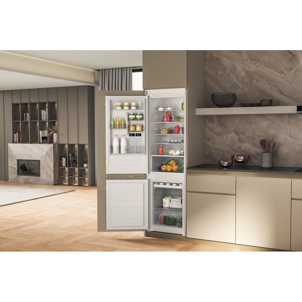 Un frigorifero aperto rivela generi alimentari. La cucina ha pavimenti in legno, un camino e un bancone con utensili.