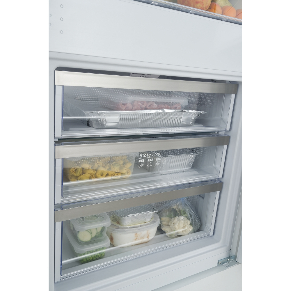 All'interno di un frigorifero bianco ci sono tre cassetti pieni di cibo: carne, pasta e verdure. Sono visibili vassoi in alluminio e contenitori di plastica.