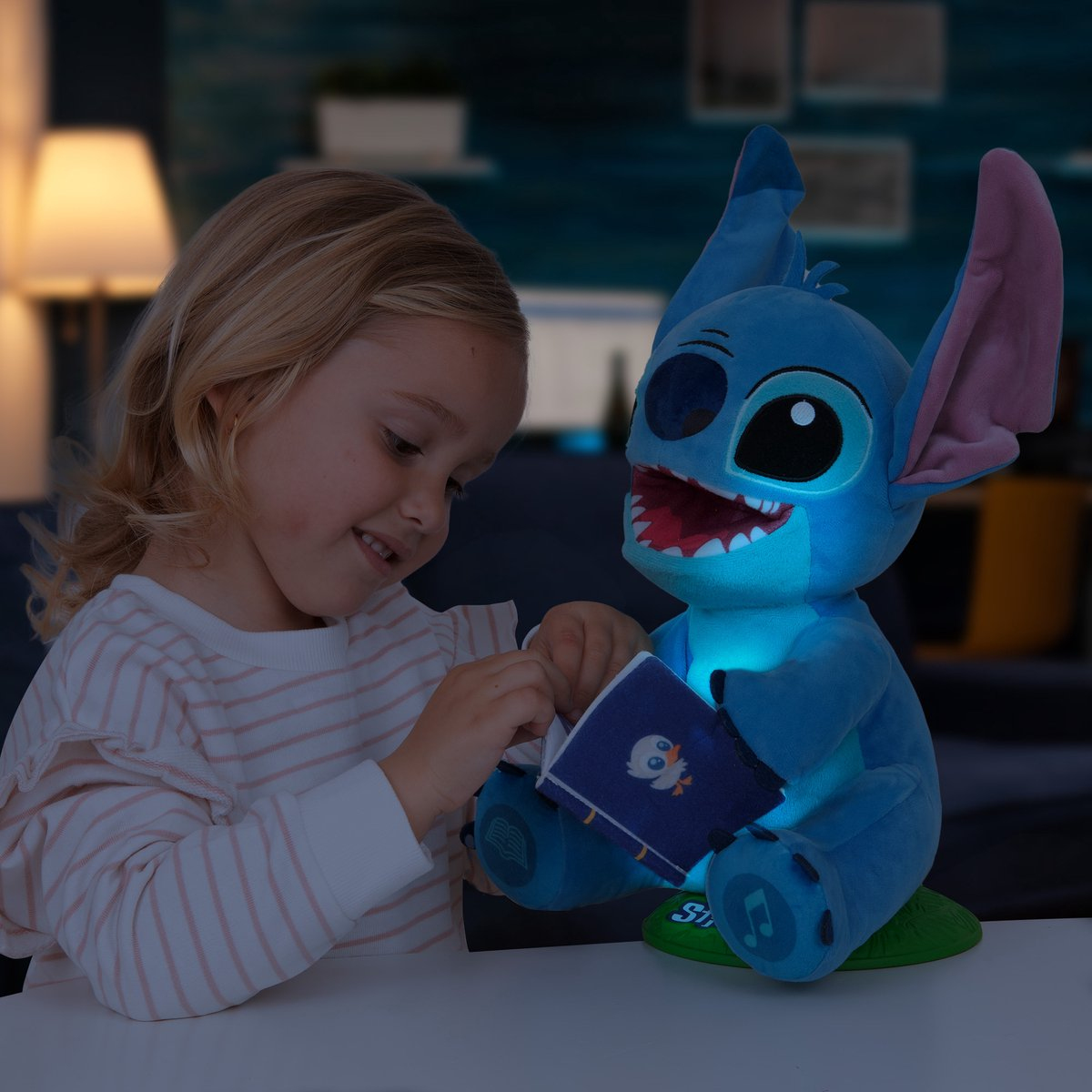 Ein Mädchen betrachtet ein leuchtendes Stitch-Plüschtier, das ein Buch hält. Das Plüschtier hat ein Licht und steht auf einer grünen Basis.