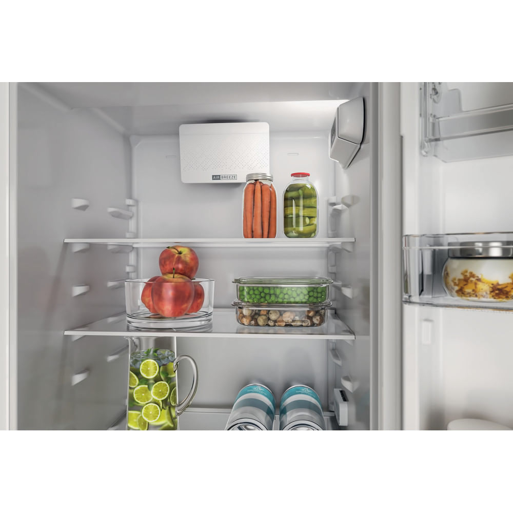 Interno di un frigorifero pieno di cibo: mele, lime, piselli, carote, sottaceti e bevande. Sono visibili scaffali.
