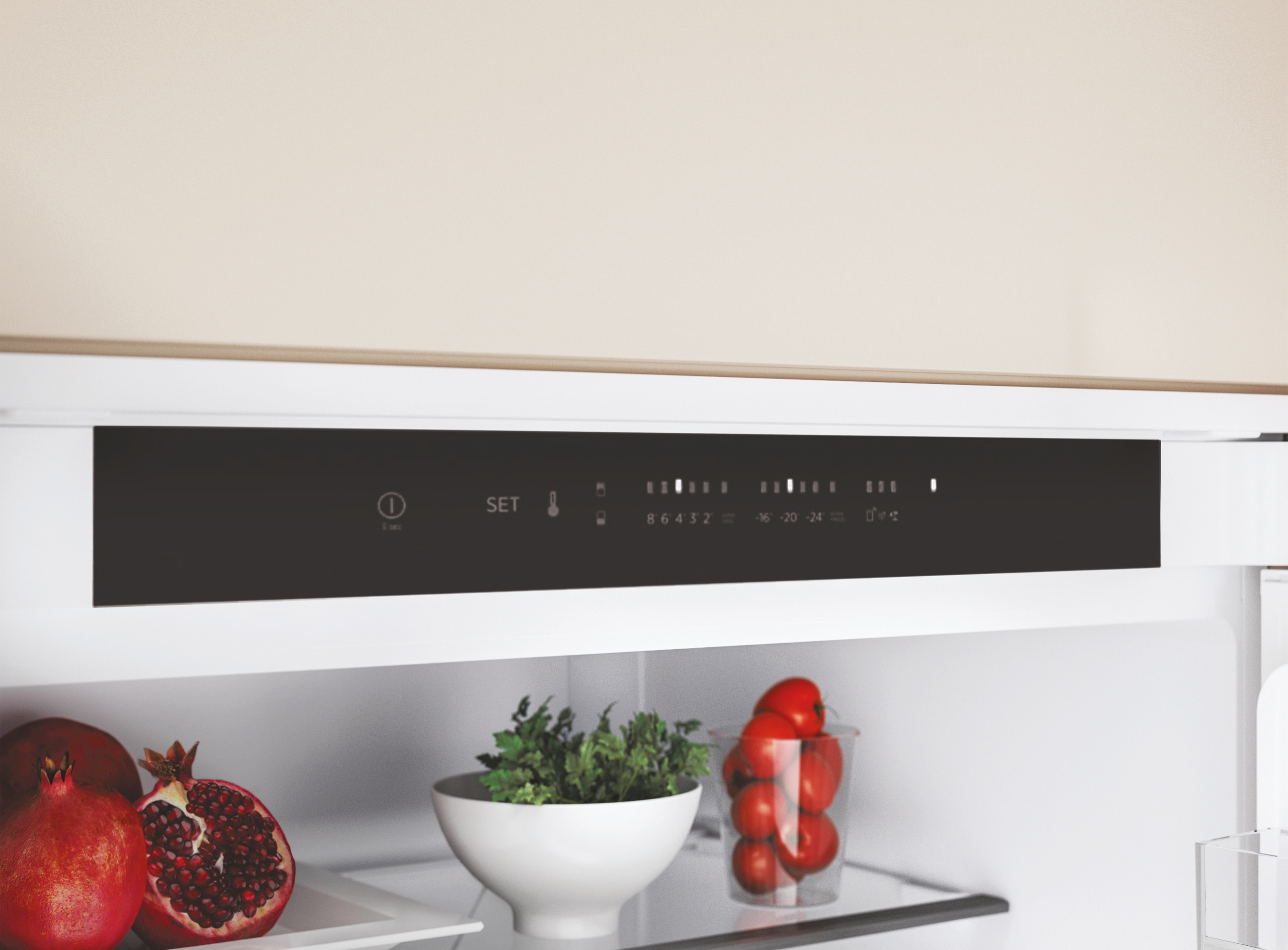 Interno del frigorifero con melograni, erbe aromatiche e pomodori. Display digitale con opzioni di impostazione. Parte superiore beige e ripiani bianchi.