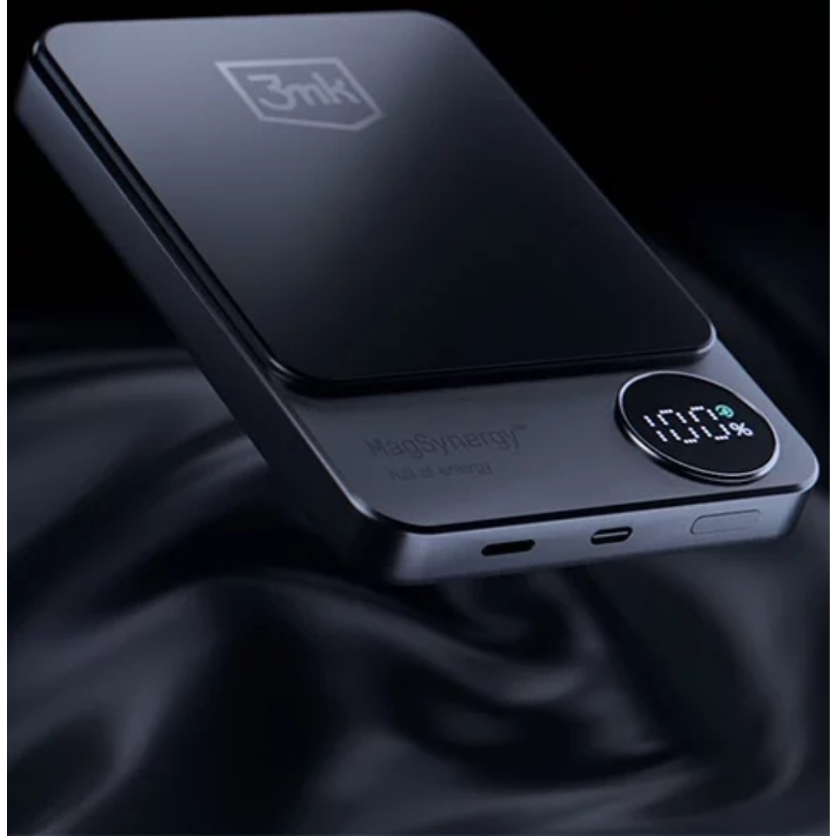 Czarny power bank z cyfrowym wyświetlaczem pokazującym 100% naładowania. Ma elegancki wygląd i jest umieszczony na ciemnej, teksturowanej powierzchni.