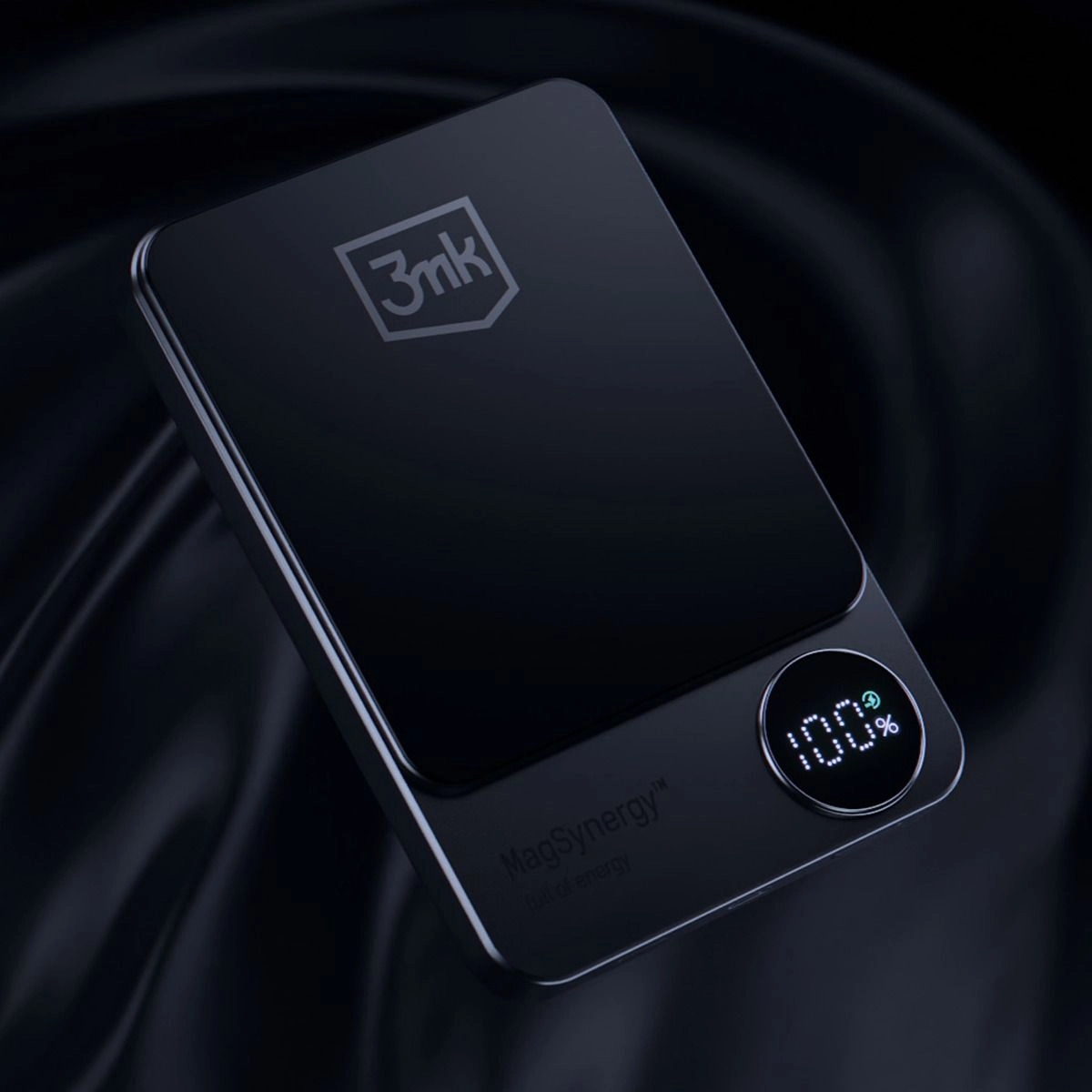 Czarny power bank z logo '3mk' i wyświetlaczem '100%'. Widoczny tekst 'MagSynergy'. Ciemne, teksturowane tło.