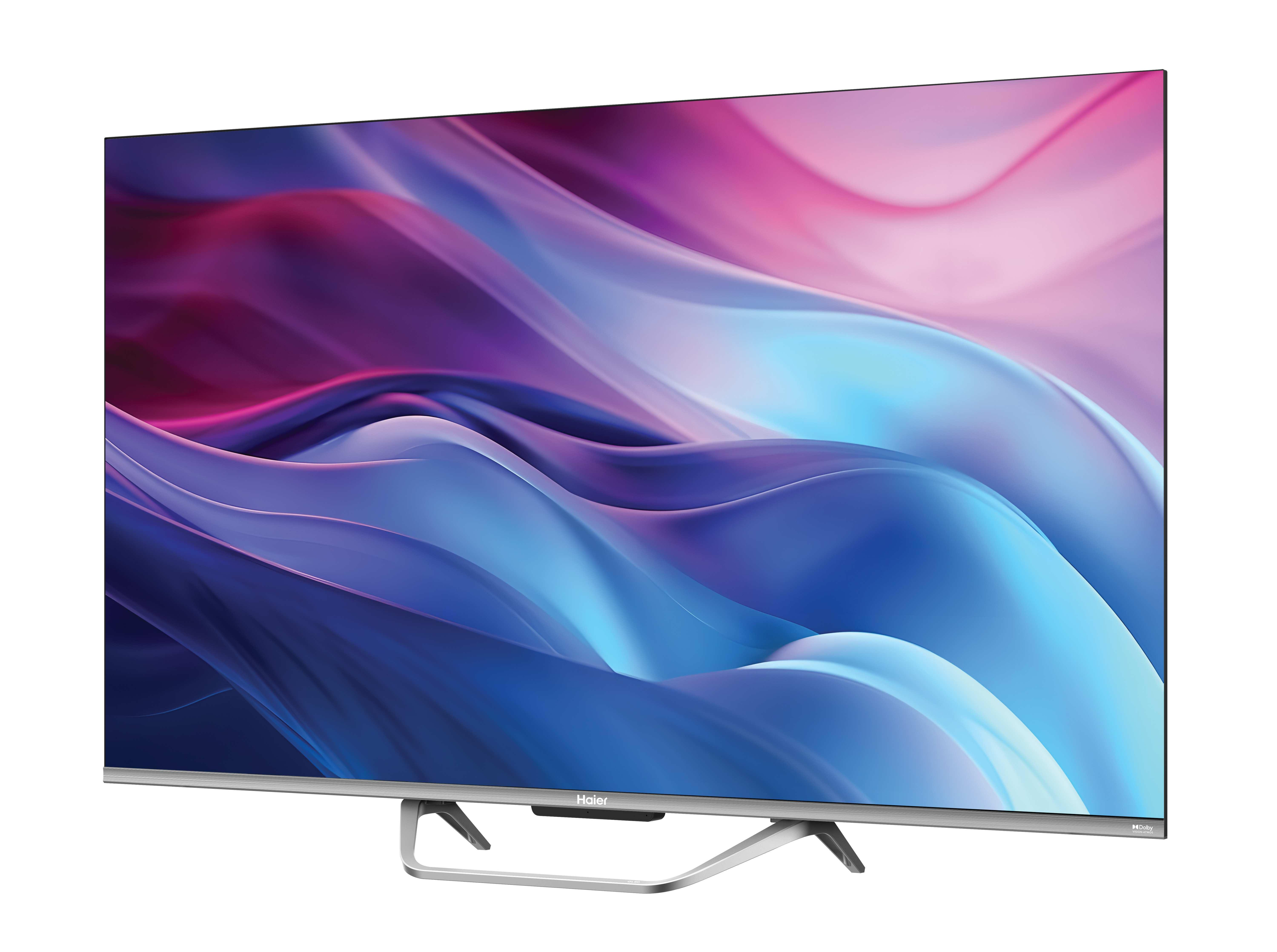Un téléviseur Haier affiche des vagues colorées abstraites. Le téléviseur a un pied et un cadre argentés. Le fond est blanc.
