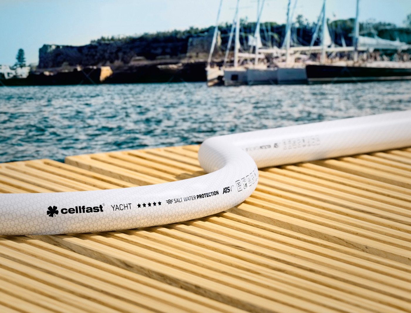 Weißer Schlauch auf Holzsteg, Meer und Boote im Hintergrund. Text "cellfast YACHT" sichtbar. Klarer sonniger Tag.