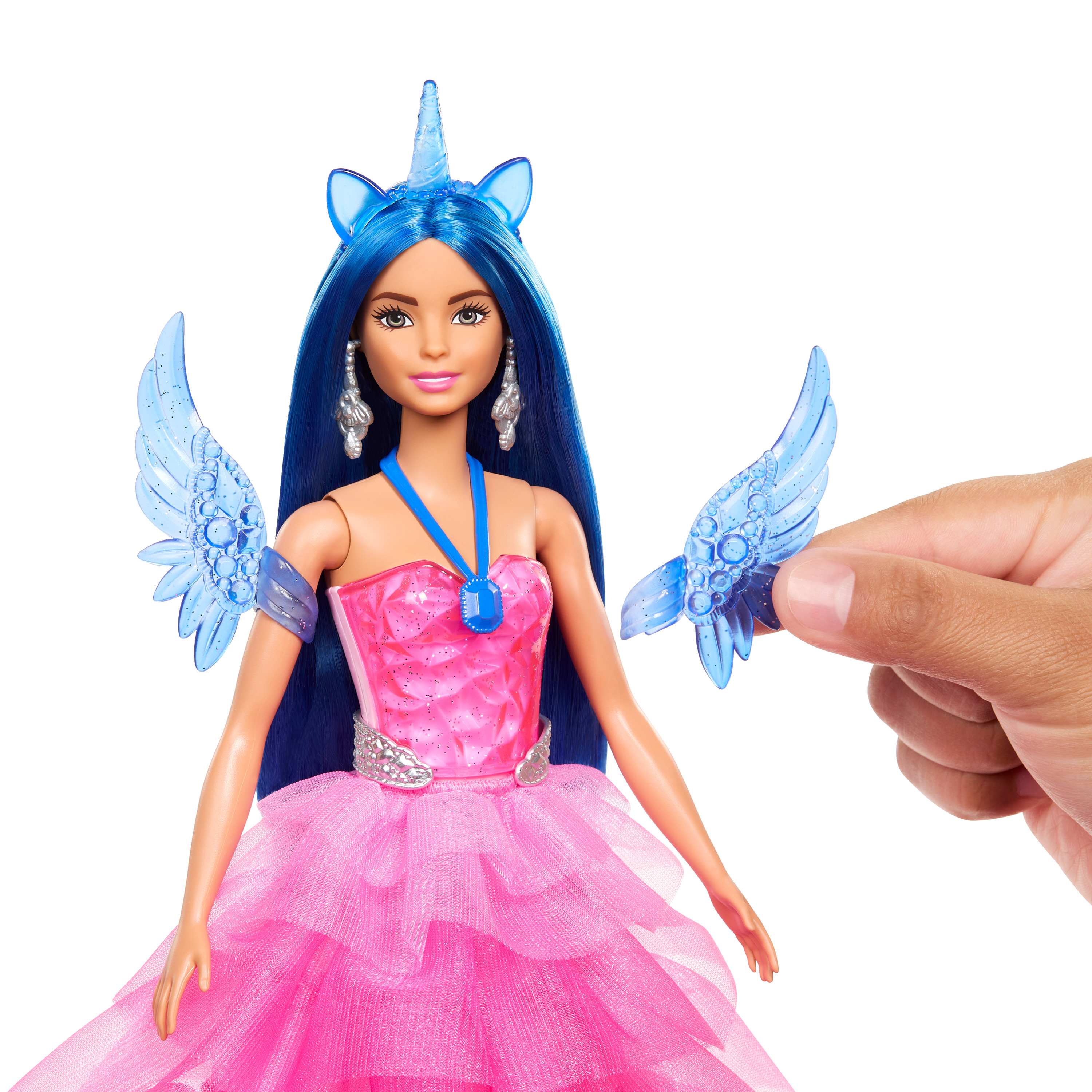 Eine Barbie-Puppe mit blauen Haaren, einem rosa Kleid und einem Einhorn-Horn. Eine Hand hält ein blaues Flügel-Zubehör.