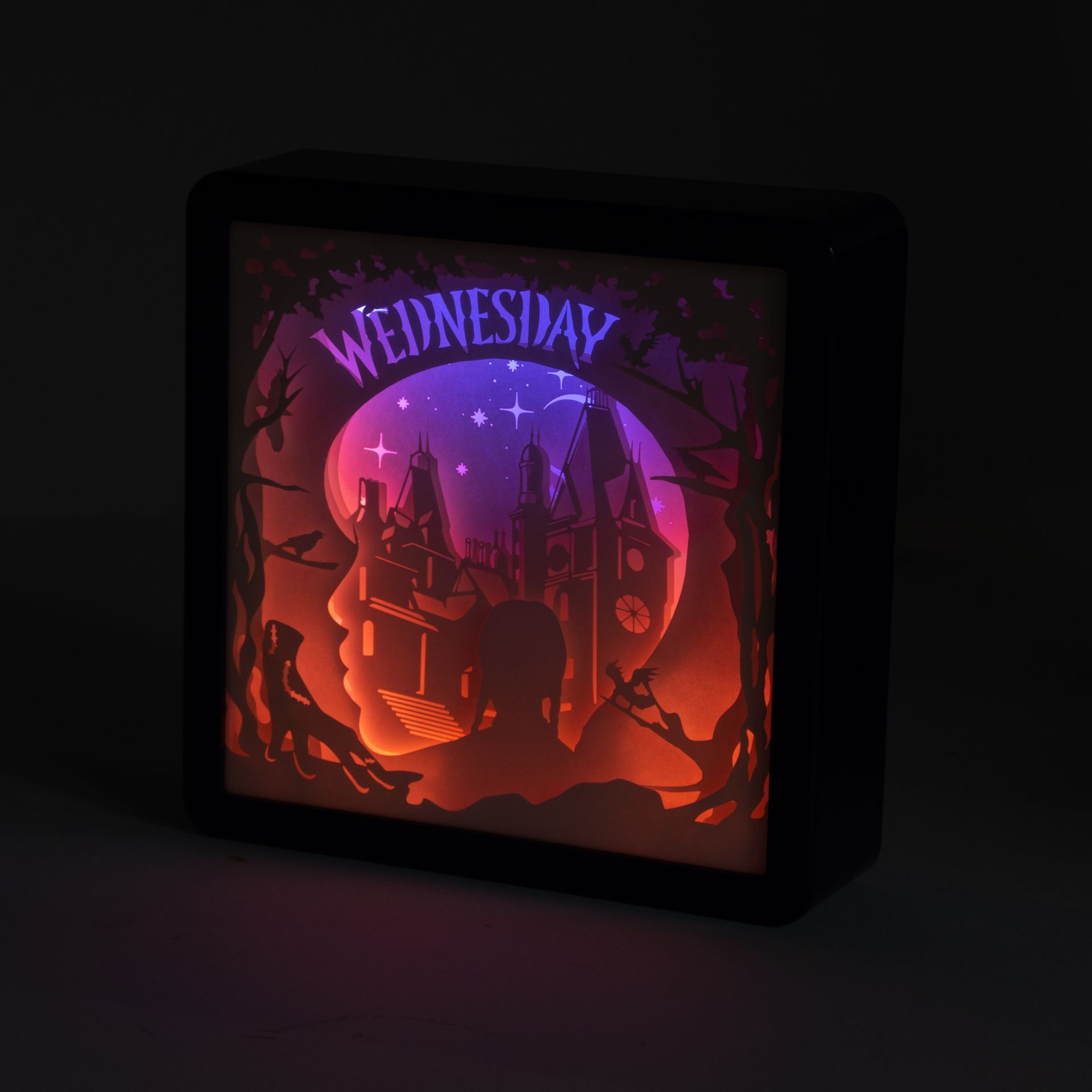 Podświetlane pudełko z sylwetką Wednesday. Ma zamek, drzewa i gwiazdy. Tekst 'Wednesday' jest na górze.