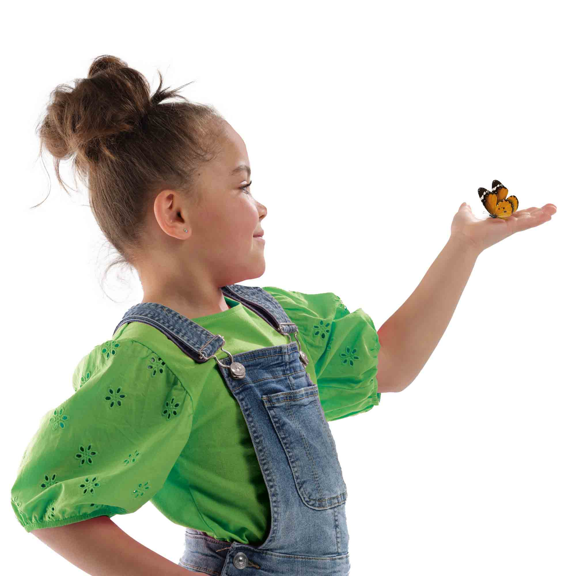 Una niña con top verde y peto vaquero mira una mariposa en su mano. Fondo blanco.