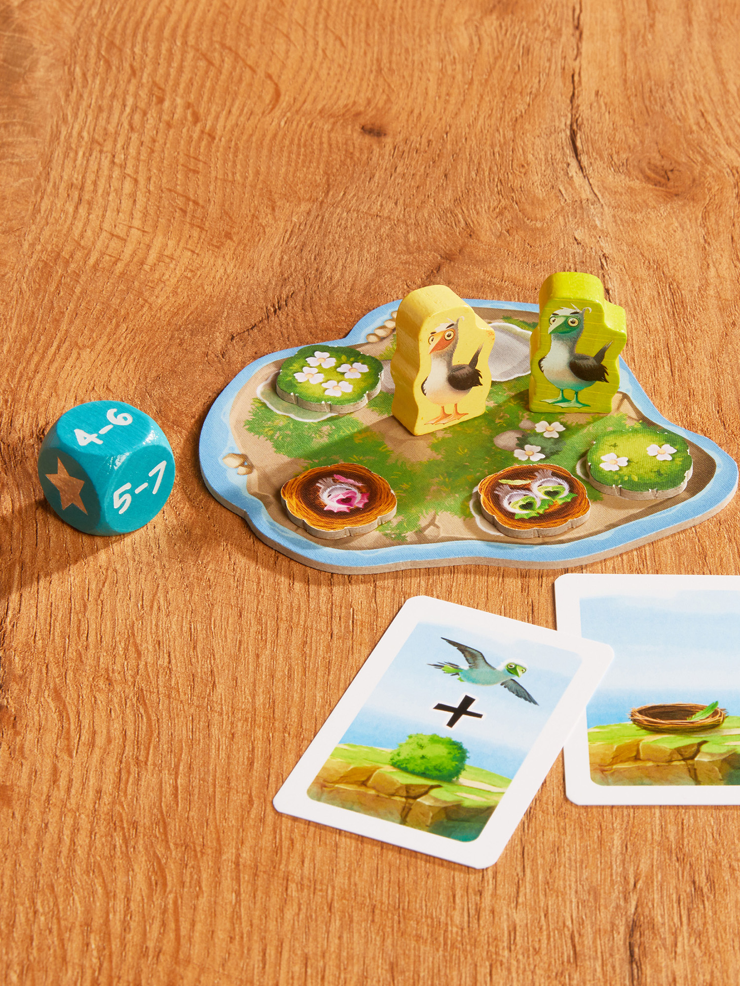 Holzspielsteine, Karten und ein Würfel liegen auf einer Holzoberfläche. Das Spiel zeigt Vögel und Nester.
