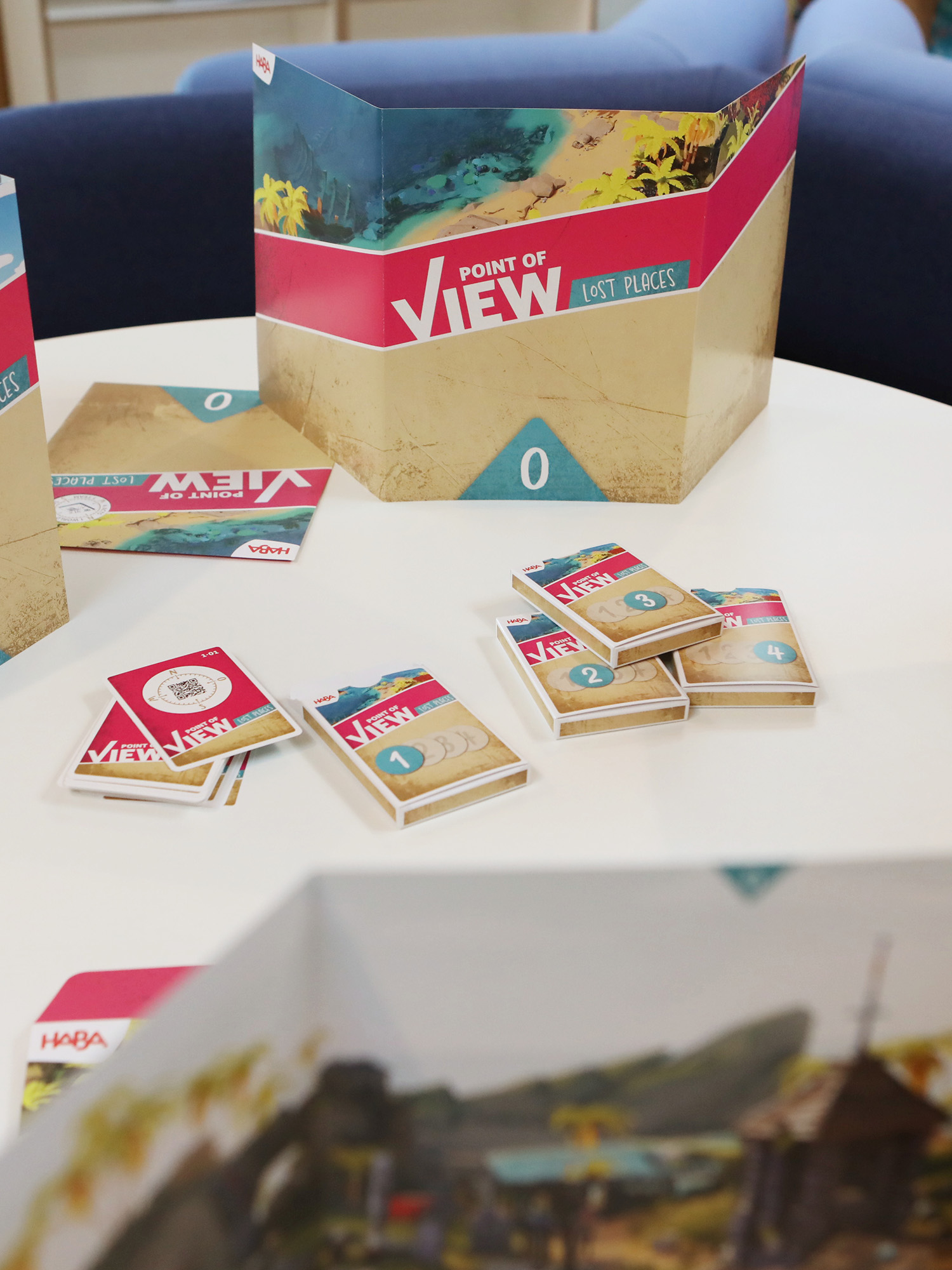 Auf einem Tisch liegt ein Brettspiel mit dem Titel 'Point of View: Lost Places'. Karten und Spielsteine liegen verstreut.