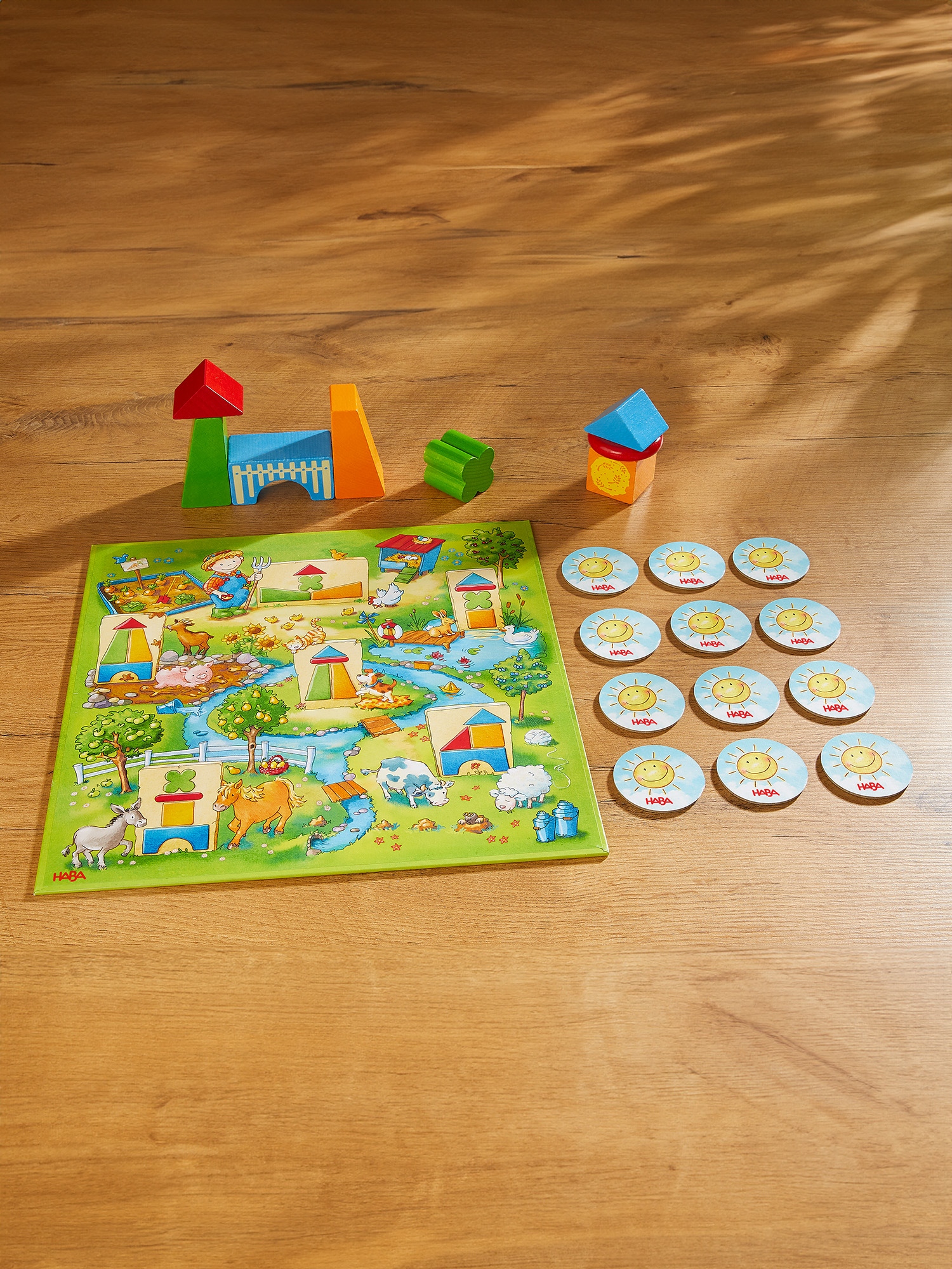Ein Holzspiel mit Bauernhof-Motiv, Blöcken, Spielbrett und sonnenförmigen Spielsteinen. Das Brett zeigt eine Bauernhofszene.
