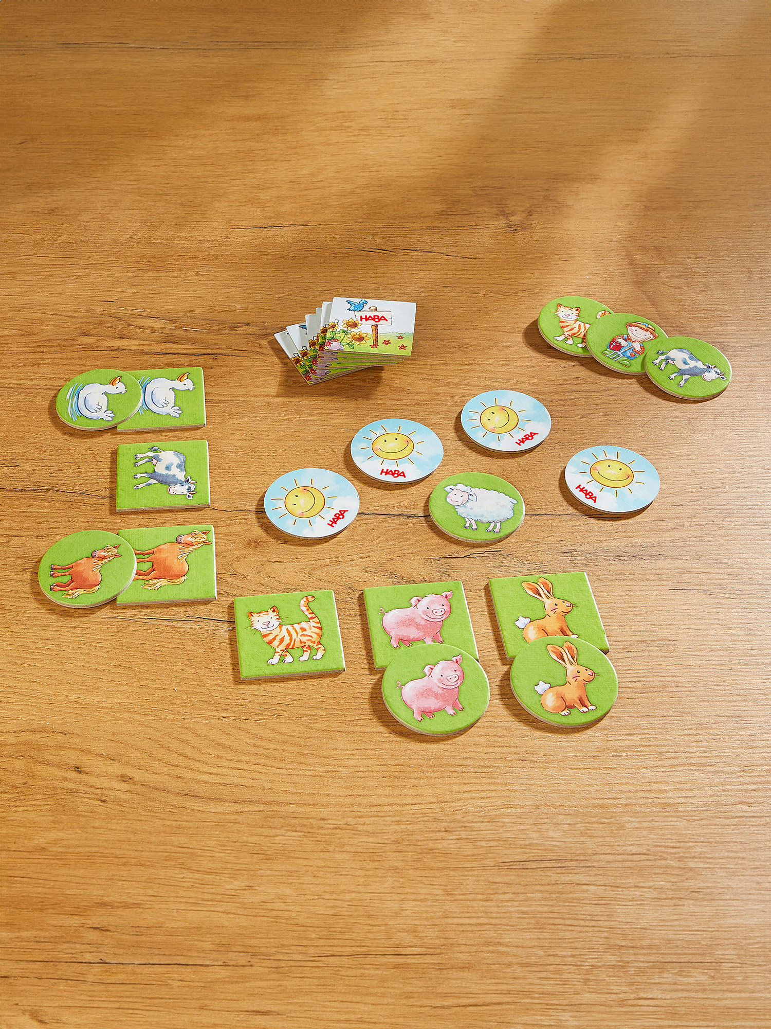 Holzoberfläche mit Spielsteinen zum Thema Tiere. Enthält Karten mit Bildern von Sonne, Schaf, Katze, Schweinen und Hasen.