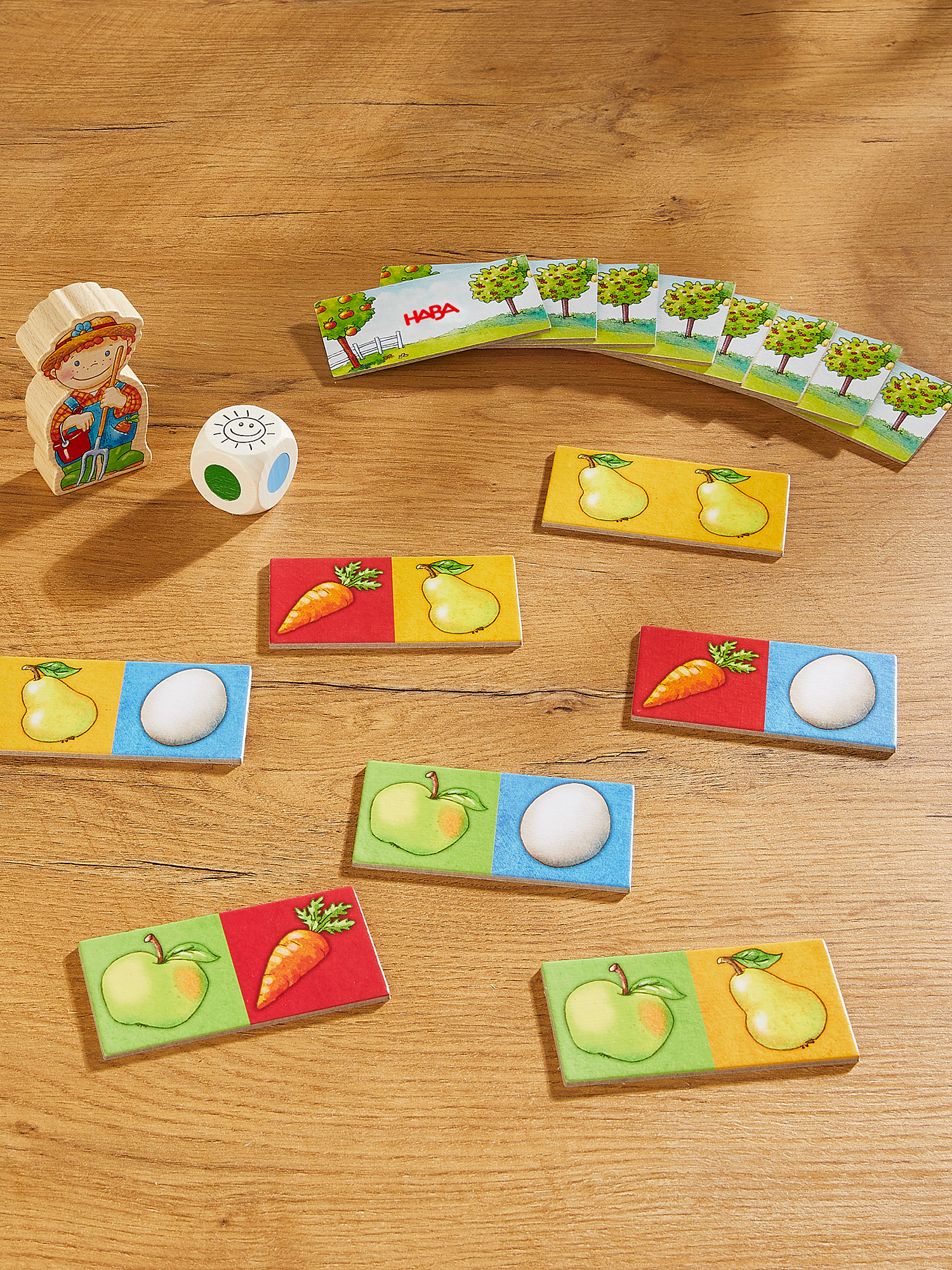 Holzbauer, Würfel, Karten mit Bäumen und Obst-/Gemüsefliesen auf Holzoberfläche. Spielkomponenten sind sichtbar.