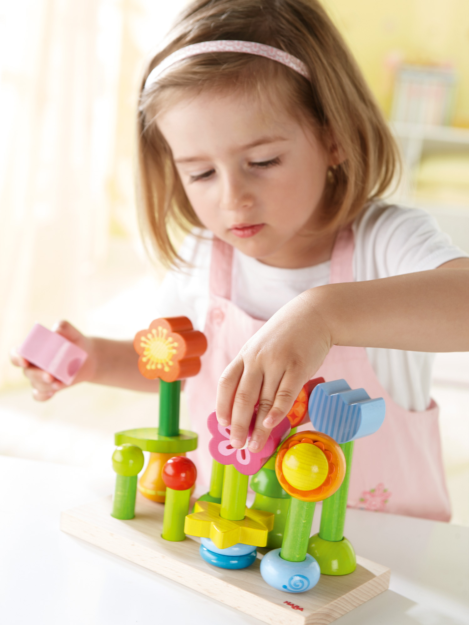 Ein junges Mädchen spielt mit einem Holzblumen-Spielzeug. Das Spielzeug hat verschiedene farbige Blumen und geometrische Formen auf grünen Stielen.