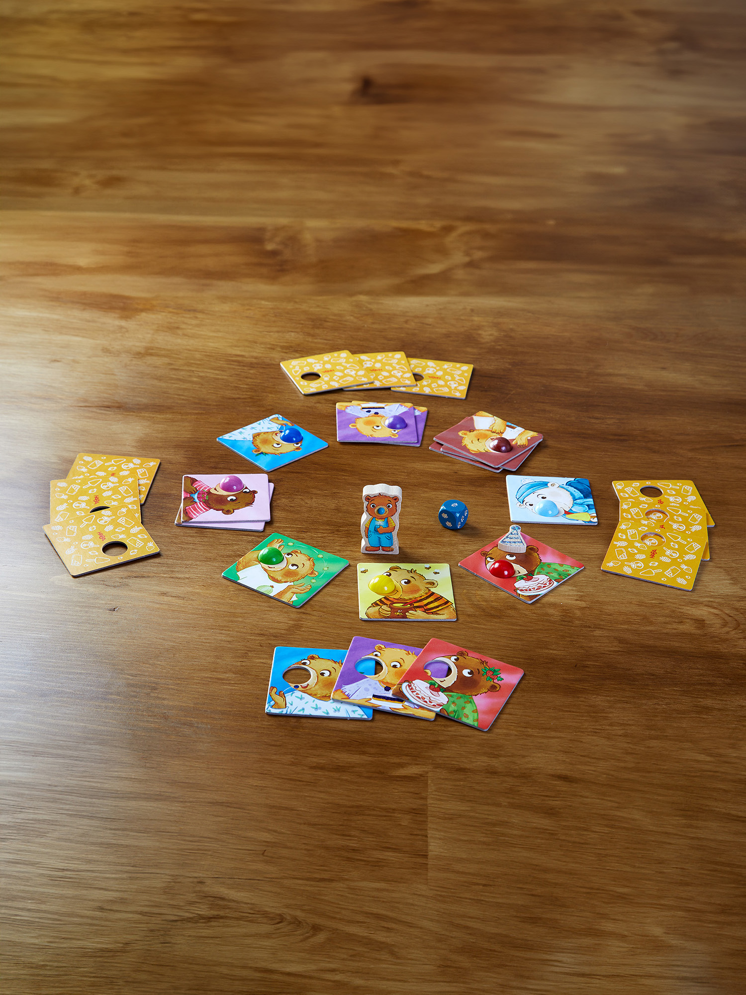 Tavolo di legno con pezzi del gioco. Carte, tessere personaggio orso, un dado e una piccola figura di orso disposti in cerchio.