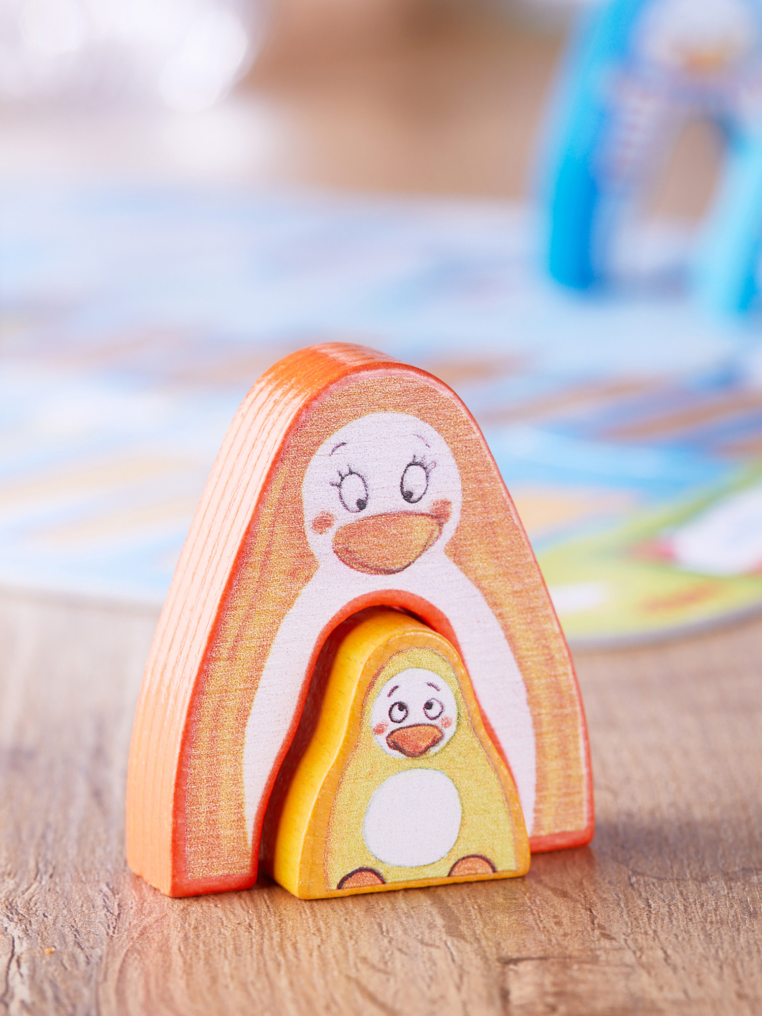 Holz-Nesting-Pinguin-Spielzeuge in Orange und Gelb auf einer Holzoberfläche. Hintergrund zeigt eine verschwommene Spielmatte.