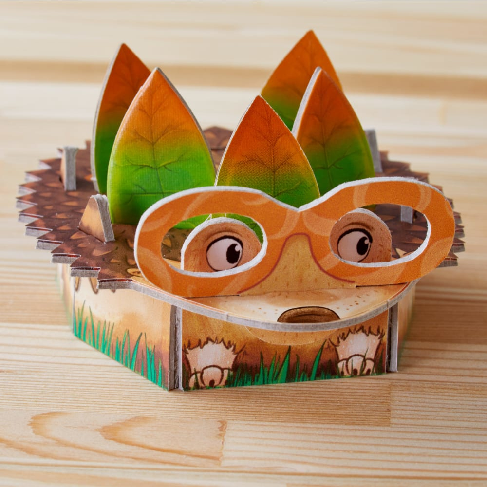 Ein Karton-Igel-Spielzeug mit blattartigen Stacheln, Brille und einem lächelnden Gesicht. Es sitzt auf einer Holzoberfläche.