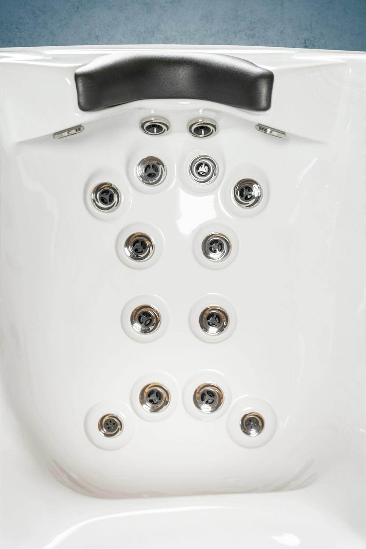 Weißes Whirlpool-Interieur mit mehreren Wasserdüsen. Oben befindet sich eine schwarze Kopfstütze. Der Hintergrund ist blau.
