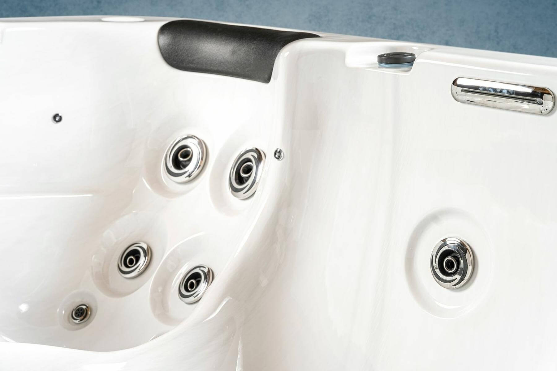 Nahaufnahme eines weißen Whirlpool-Innenraums. Mit mehreren Düsen, Chromakzenten und einer schwarzen Kopfstütze. Der Hintergrund ist blau.