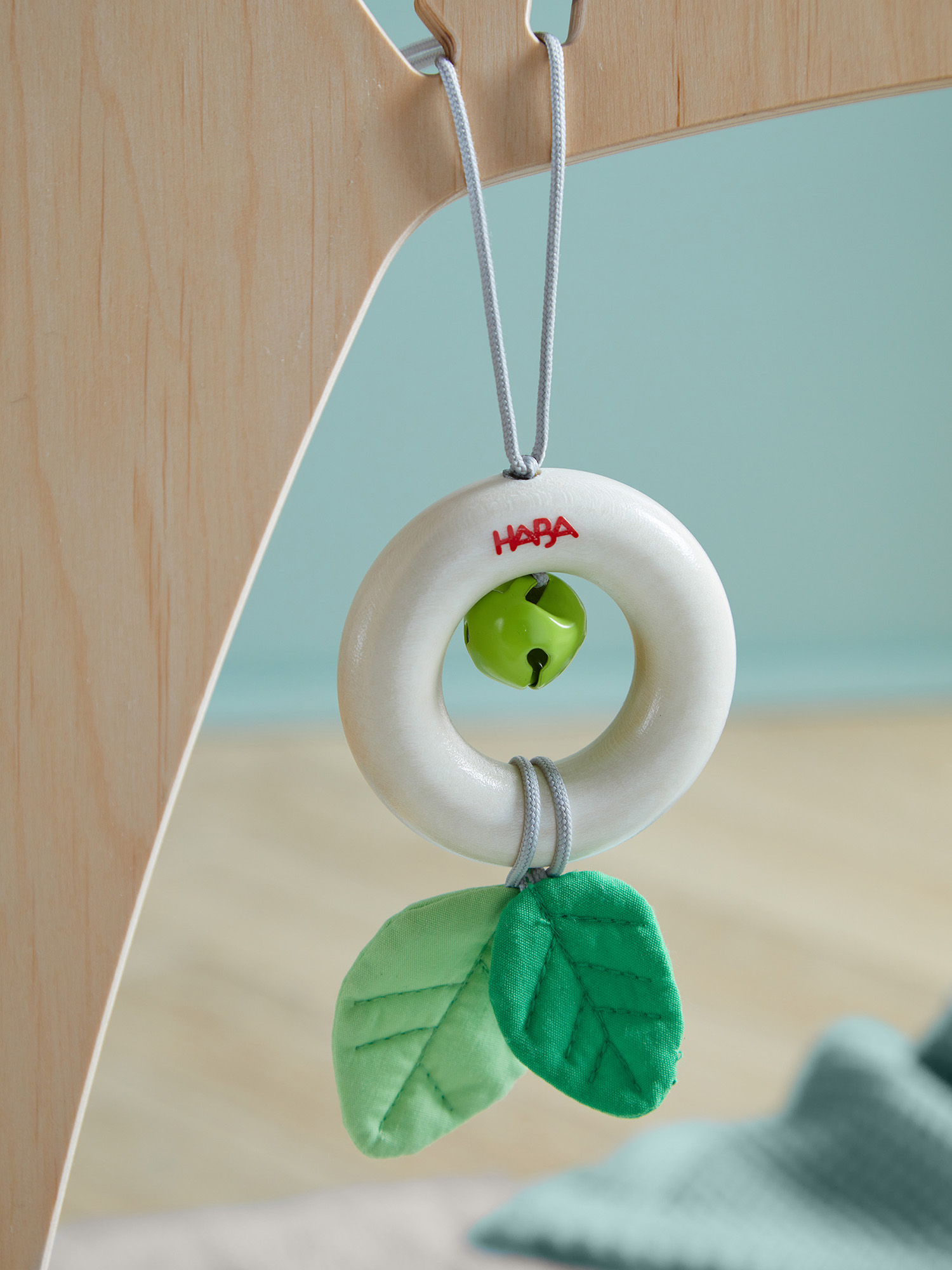 Ein Holzspielzeug für Babys mit einem weißen Ring mit der Aufschrift 'HABA', einer grünen Glocke und grünen blattförmigen Verzierungen.