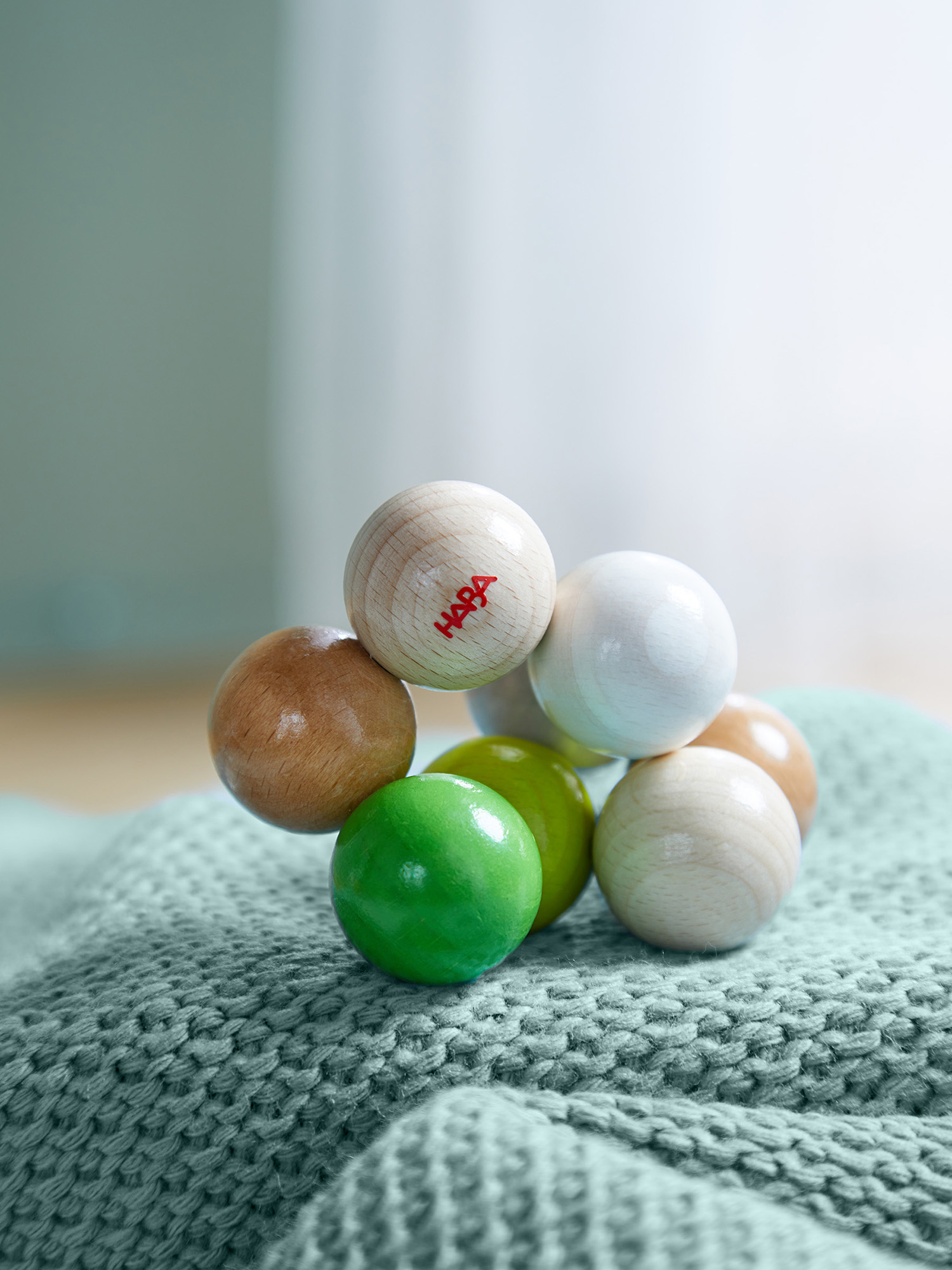 Holzspielzeug mit verschiedenfarbigen Kugeln, einige mit Markennamen. Es liegt auf einer grünen Strickdecke. Weicher Hintergrund.